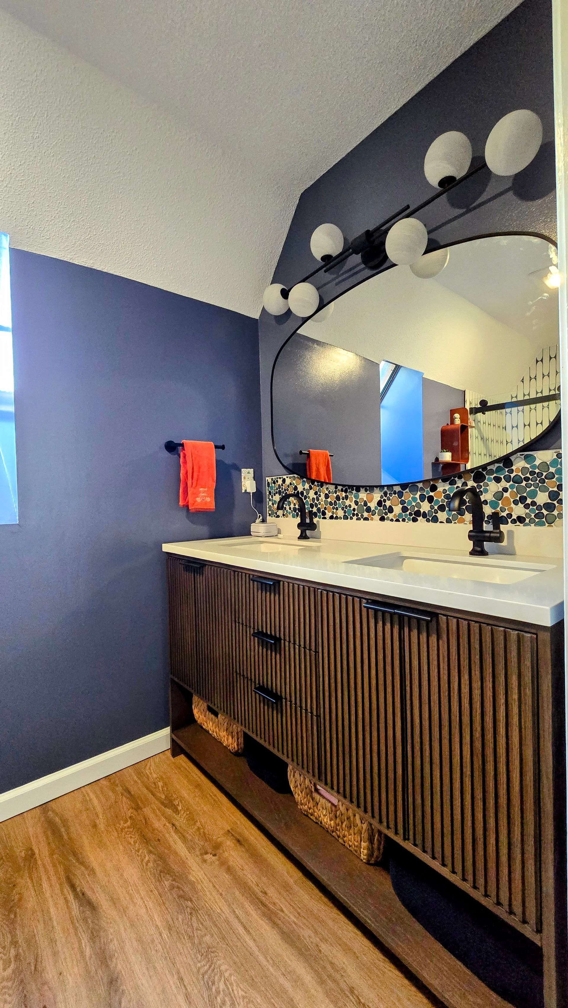 Bathroom vanity with blue walls, round mirror lights, and wood cabinet under a white countertop. By First Choice Bathroom Remodeling done in Bristol, CT.