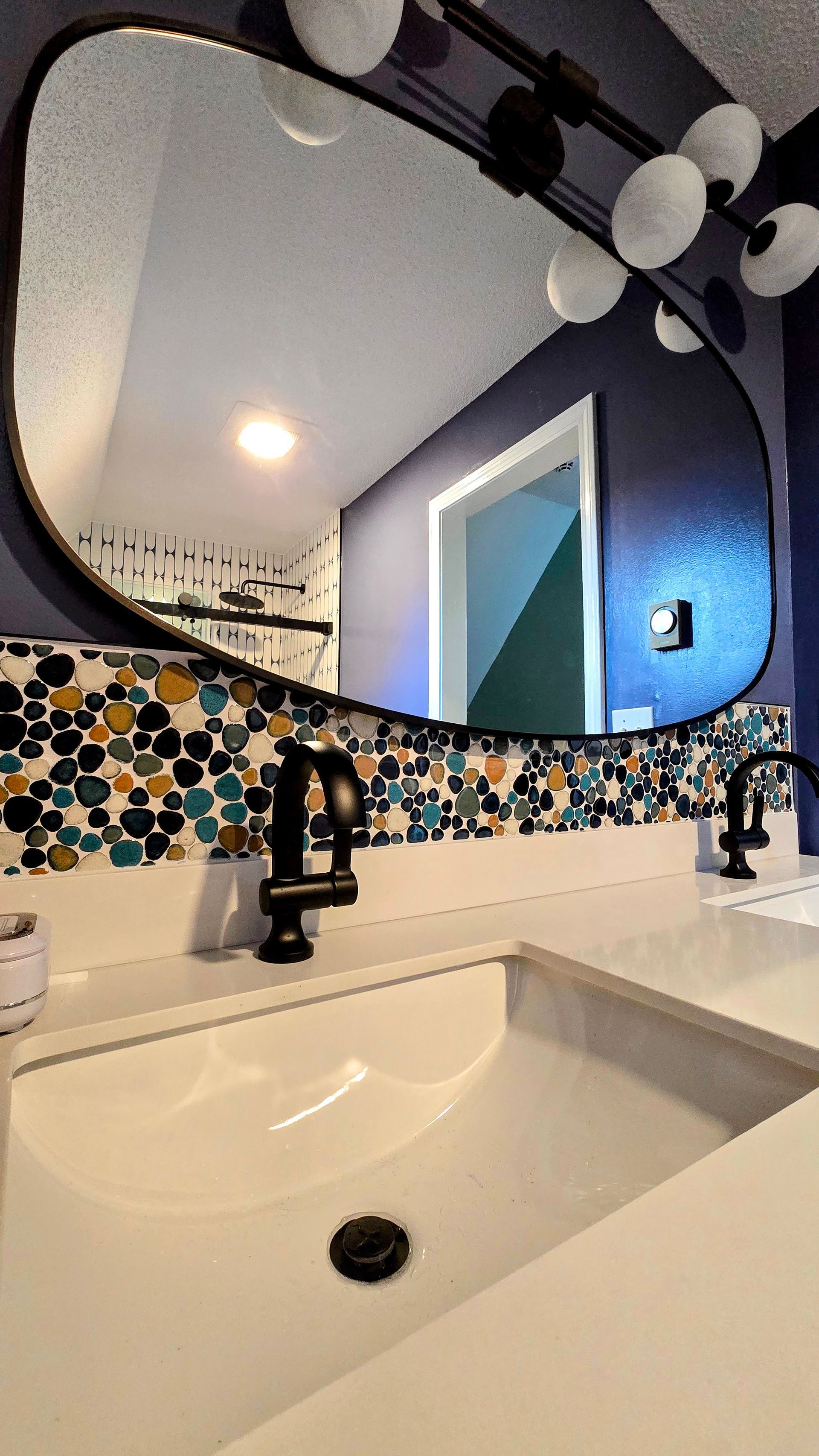Bathroom vanity with white sink, mosaic tile backsplash, round mirror, and blue accent lighting. By First Choice Bathroom Remodeling done in Bristol, CT.