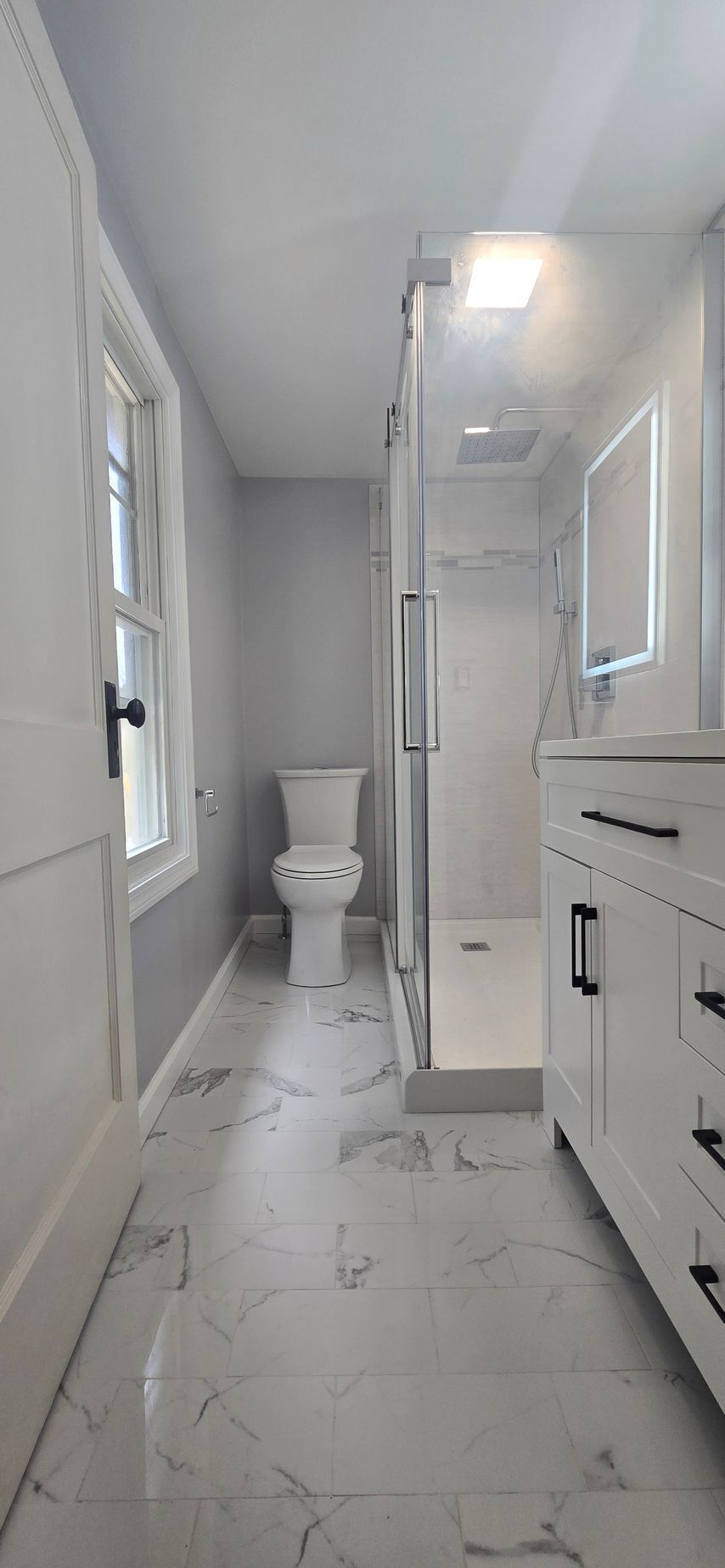 Bright white bathroom with toilet, glass shower, vanity, and marble-look tile floor. By First Choice Bathroom Remodeling done in Norfolk, CT.