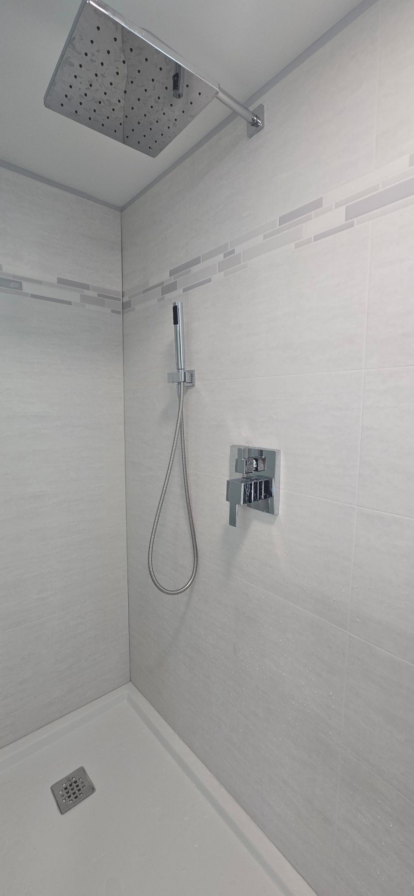 Minimal white shower stall with overhead shower, handheld sprayer, and floor drain. By First Choice Bathroom Remodeling done in Norfolk, CT.