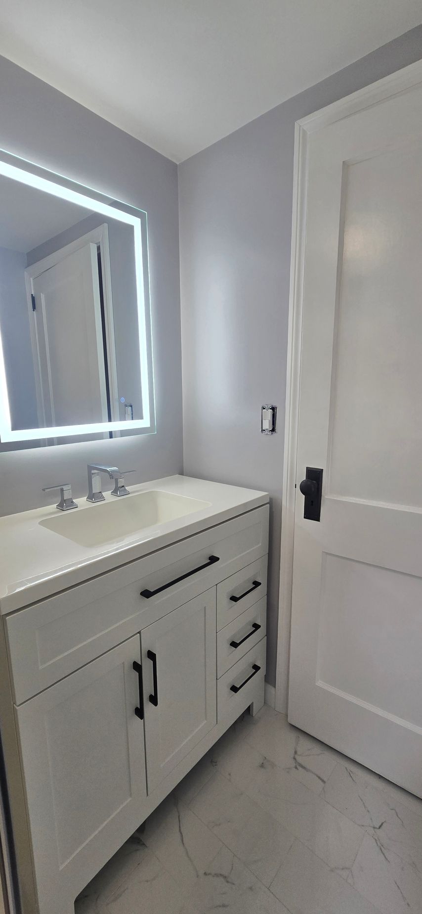 Modern bathroom vanity with white sink, mirror, and door in a light gray interior. By First Choice Bathroom Remodeling done in Norfolk, CT.