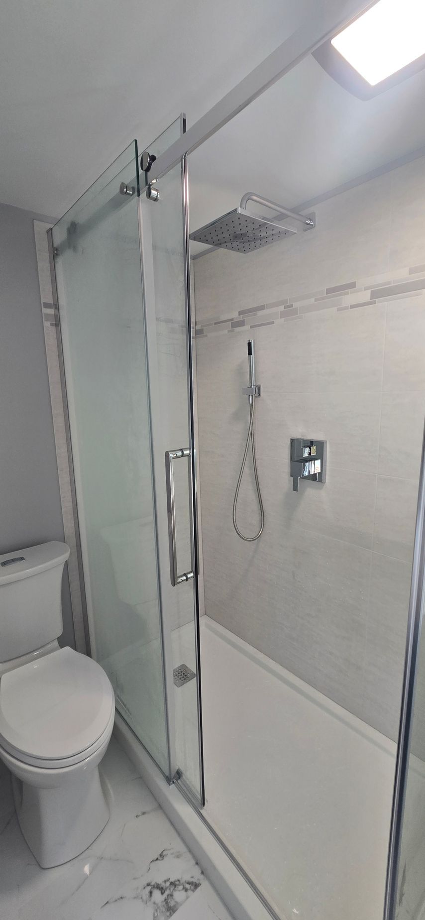 Compact bathroom with glass shower enclosure, wall-mounted showerhead, and toilet. By First Choice Bathroom Remodeling done in Norfolk, CT.