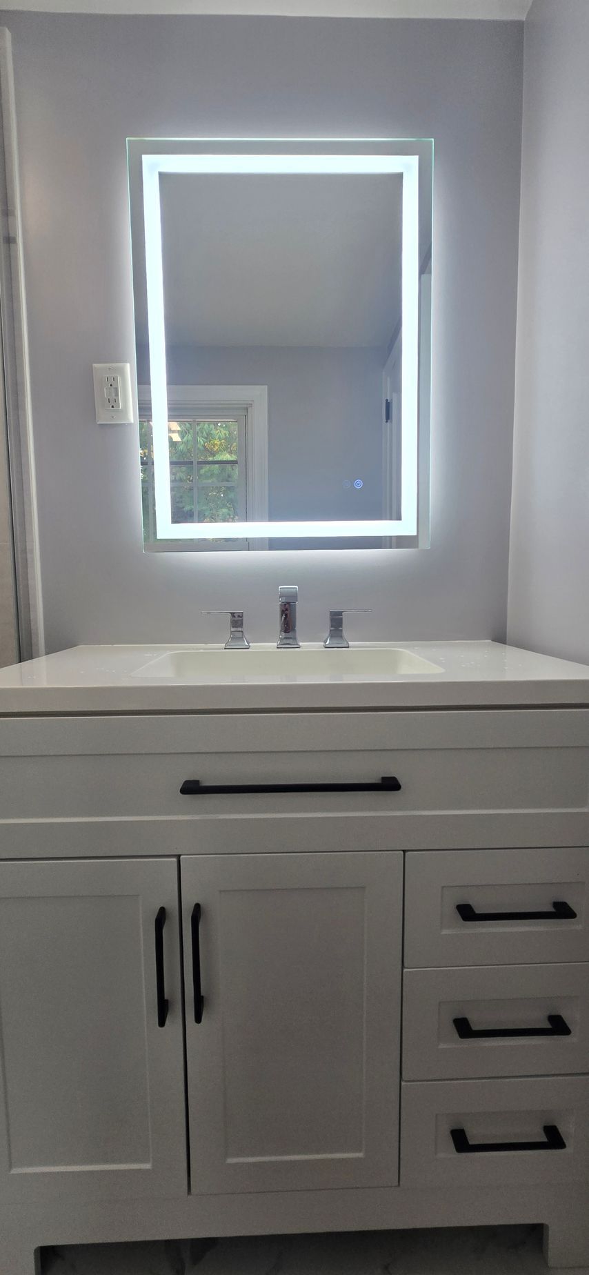 White bathroom vanity with sink and lit mirror above, shown against a gray wall. By First Choice Bathroom Remodeling done in Norfolk, CT.