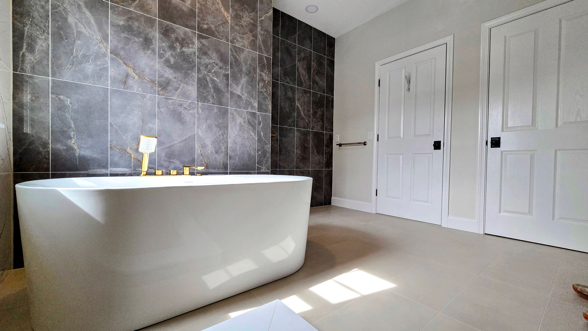 A modern bathroom in Cromwell, CT featuring a white freestanding bathtub against a dark, industrial-style tiled accent wall.