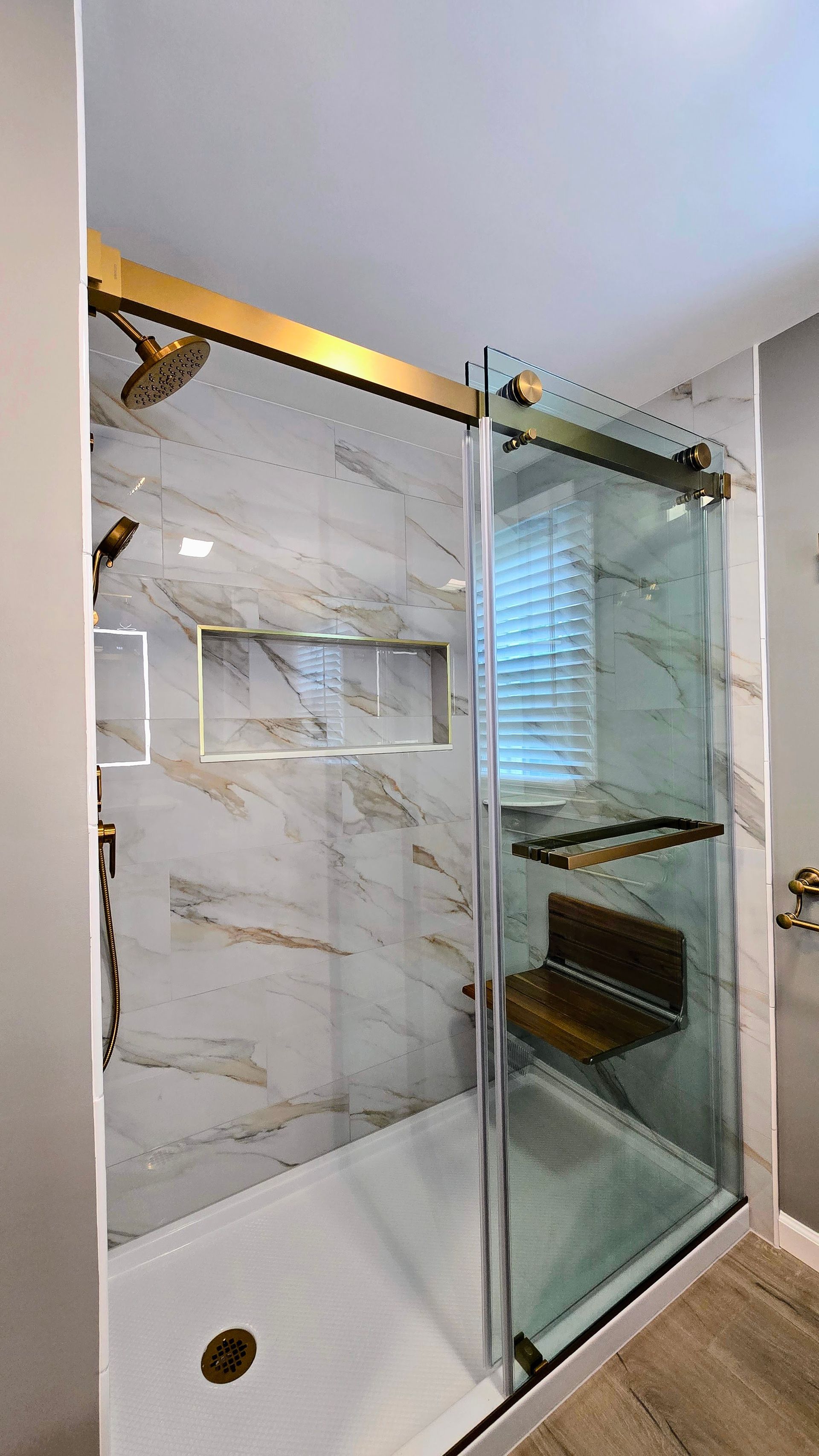 Modern bathroom with a glass shower enclosure, white marble walls, and wood flooring
