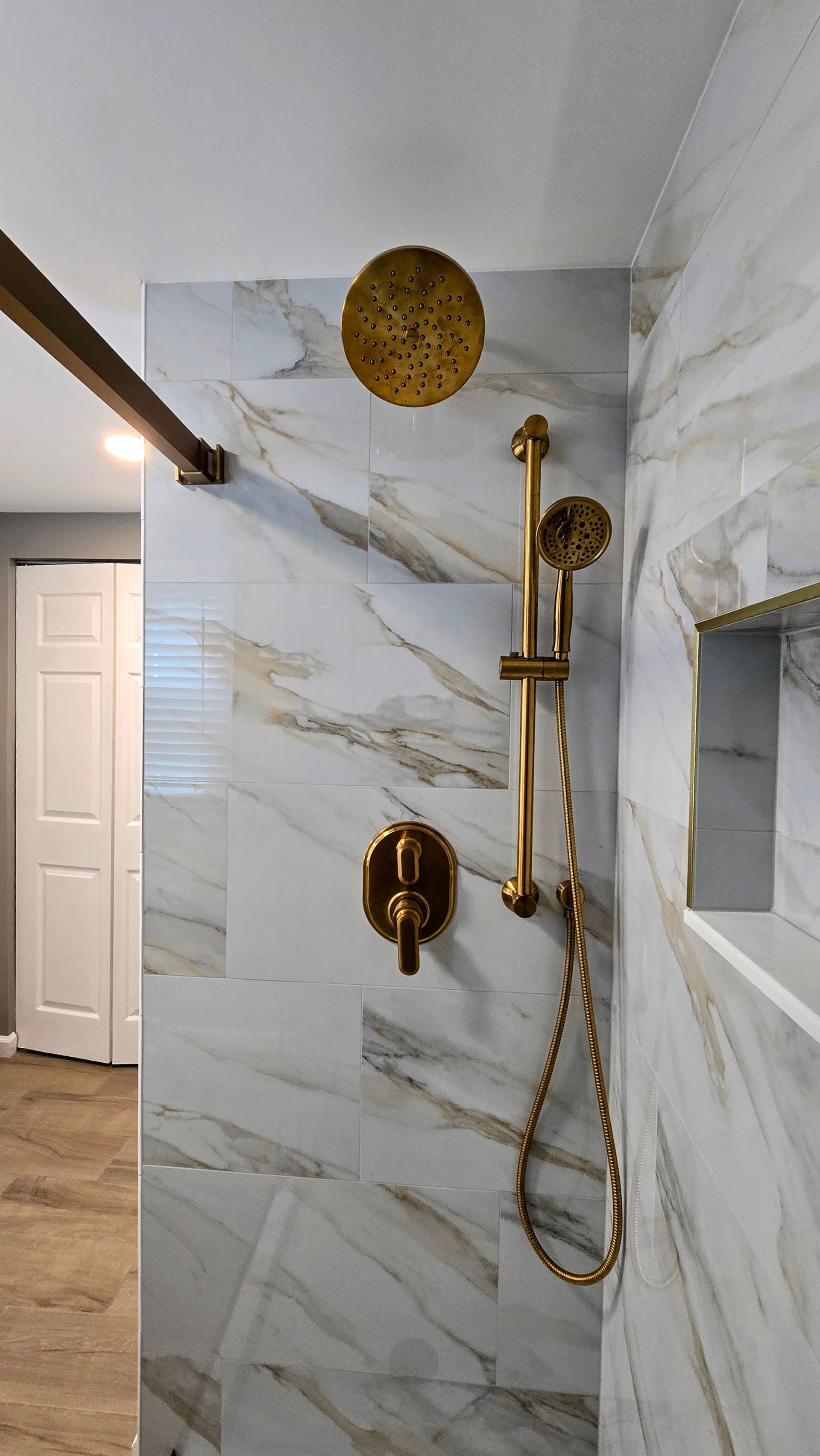 Modern bathroom shower in Southington, CT with gold fixtures, white marble-pattern tile, and a round gold wall accent