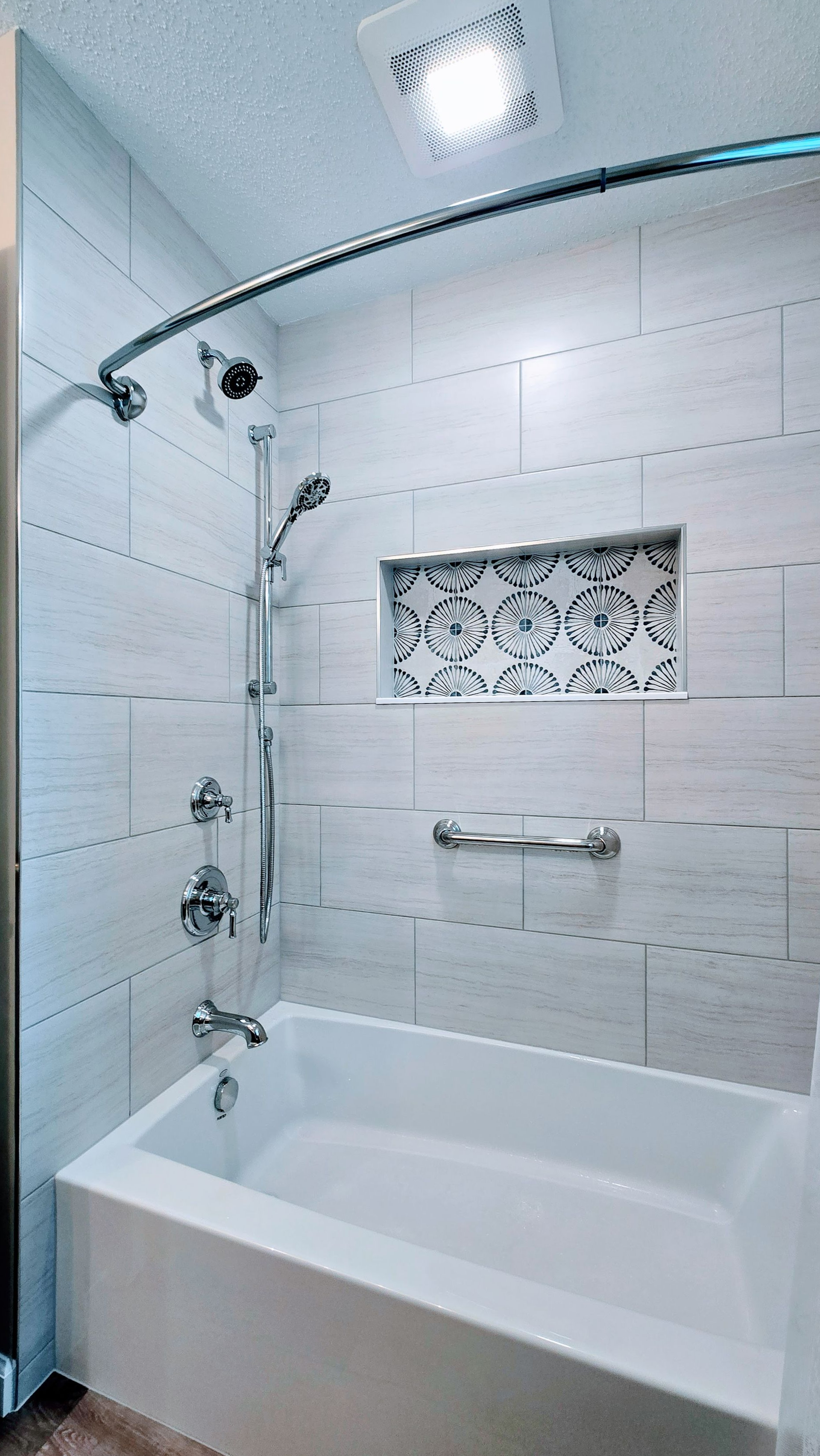 White tiled shower with a bathtub, hand shower, recessed shelf, and arched shower rod.