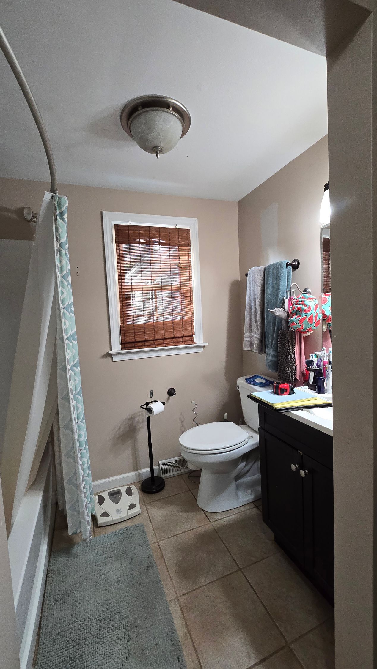 Small bathroom with toilet, sink, tiled floor, window blinds, and a ceiling light.