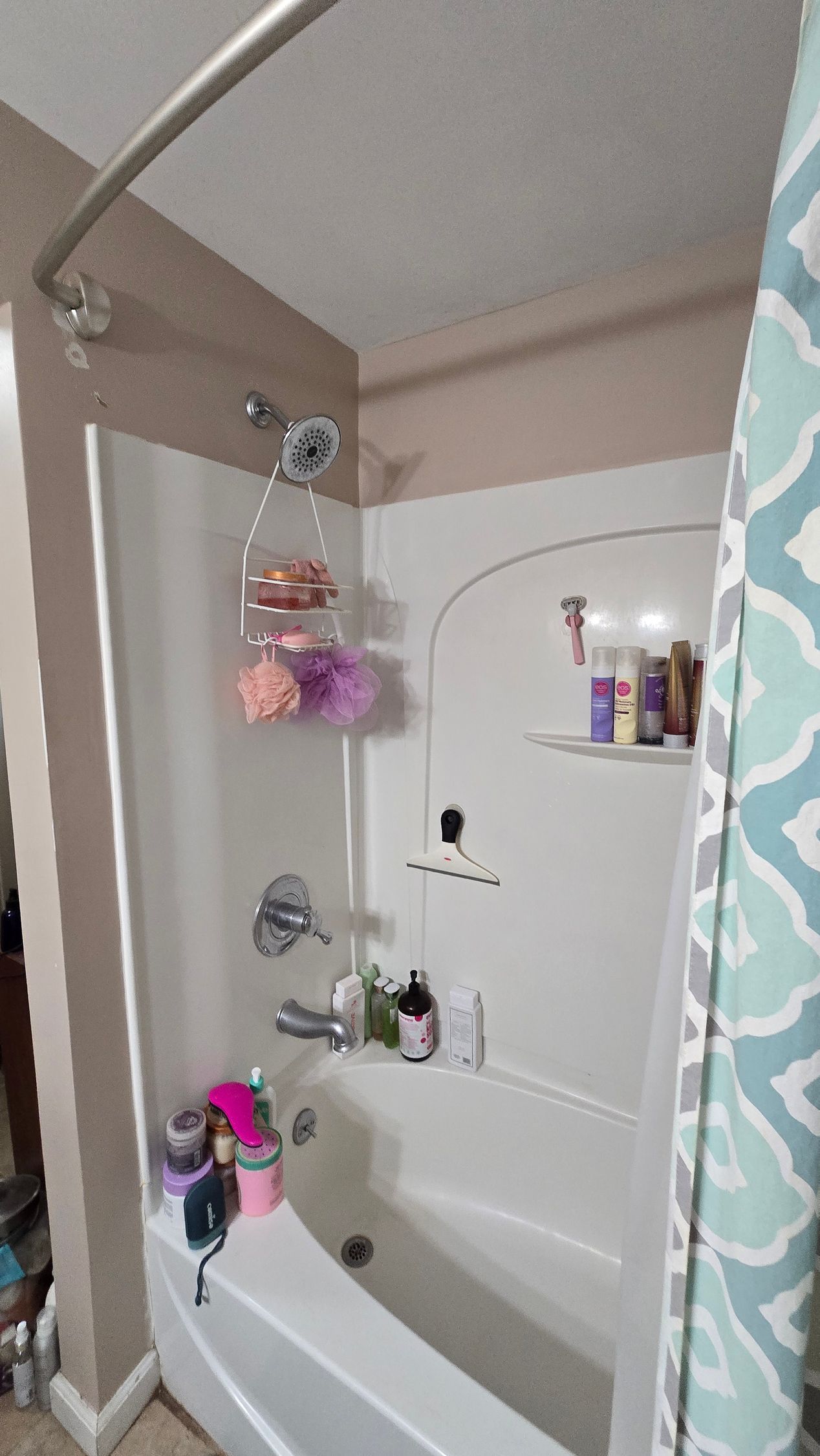 Small bathroom shower and tub with pink decor, wall shelf, and toiletries on the ledge