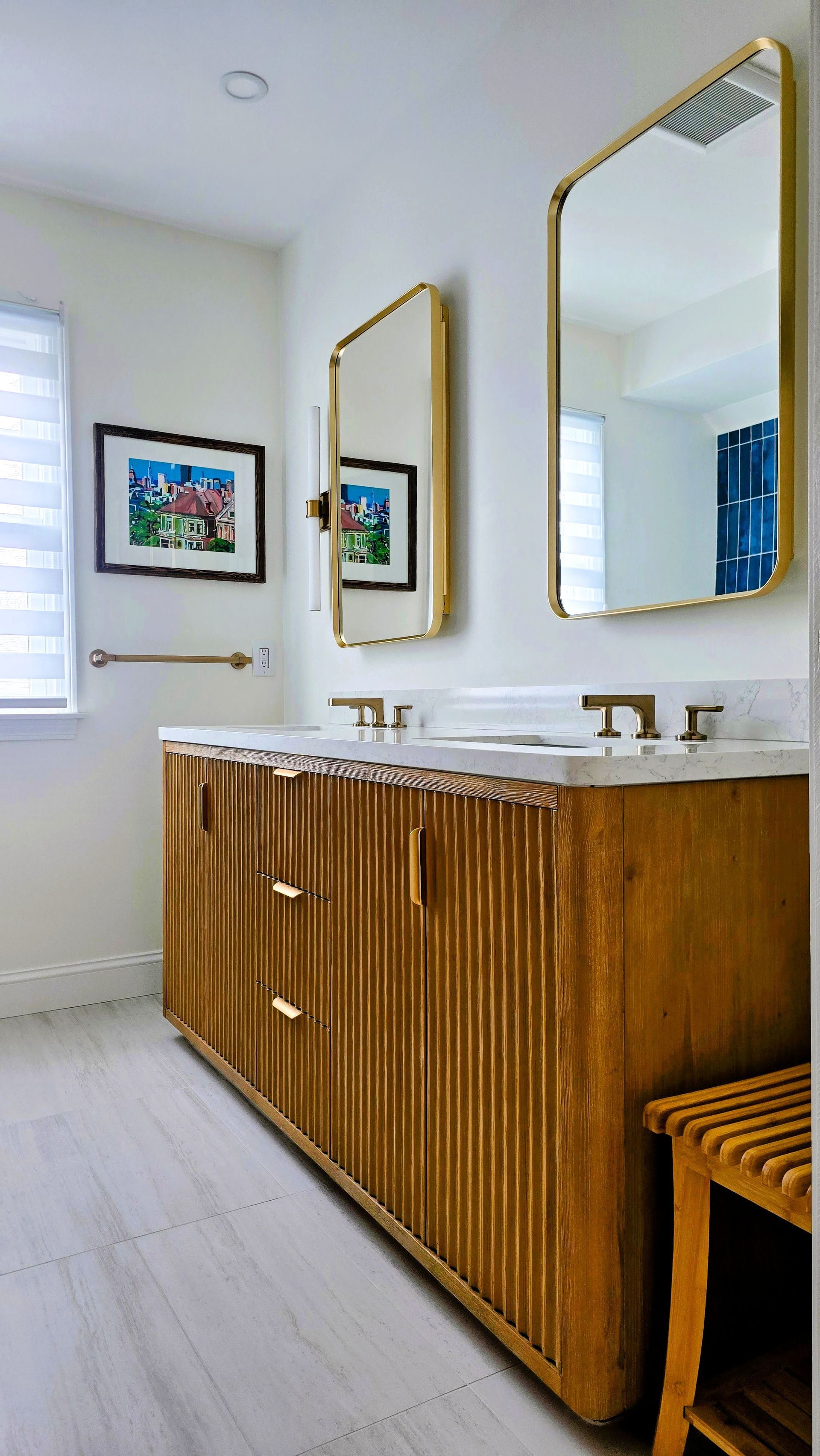 A bathroom vanity with a fluted wooden cabinet, gold fixtures, and two rectangular mirrors on a white wall.
