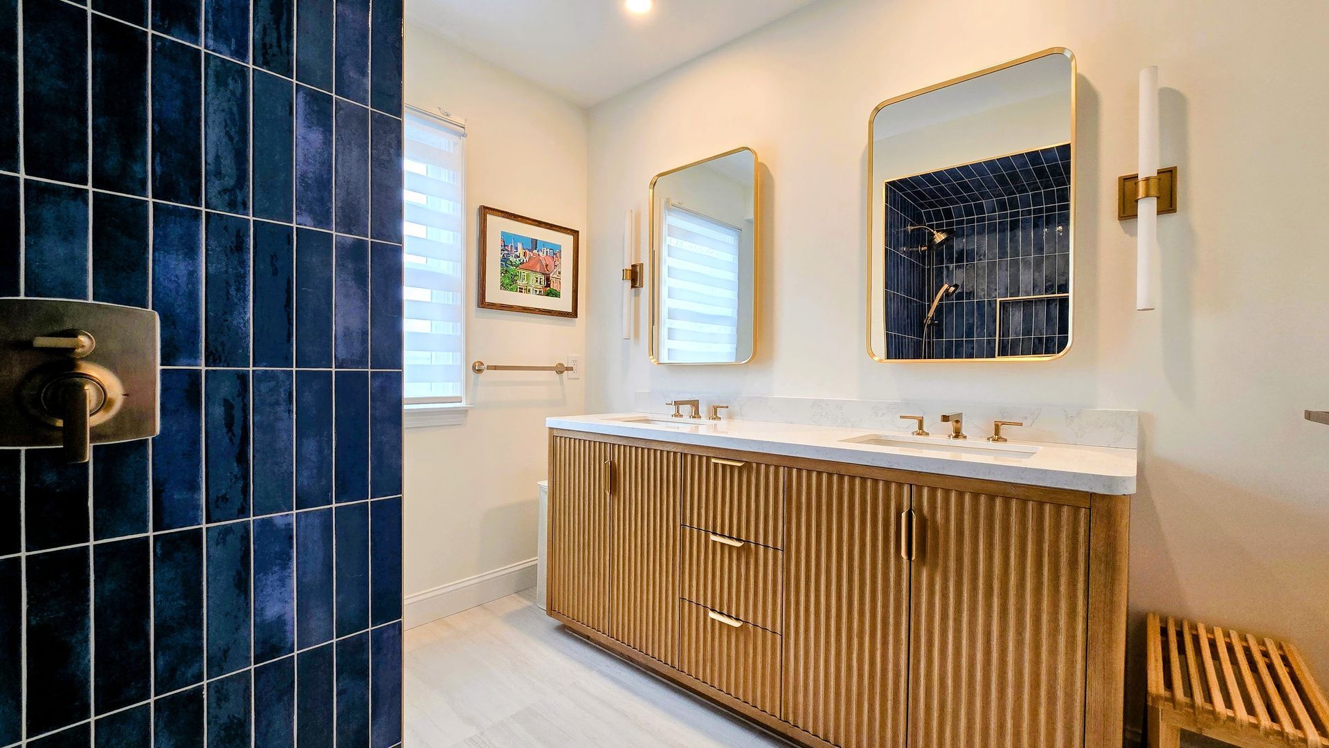 Modern bathroom in Cromwell, CT with a fluted wood double vanity, brass fixtures, two rectangular mirrors, and blue tiled shower wall.