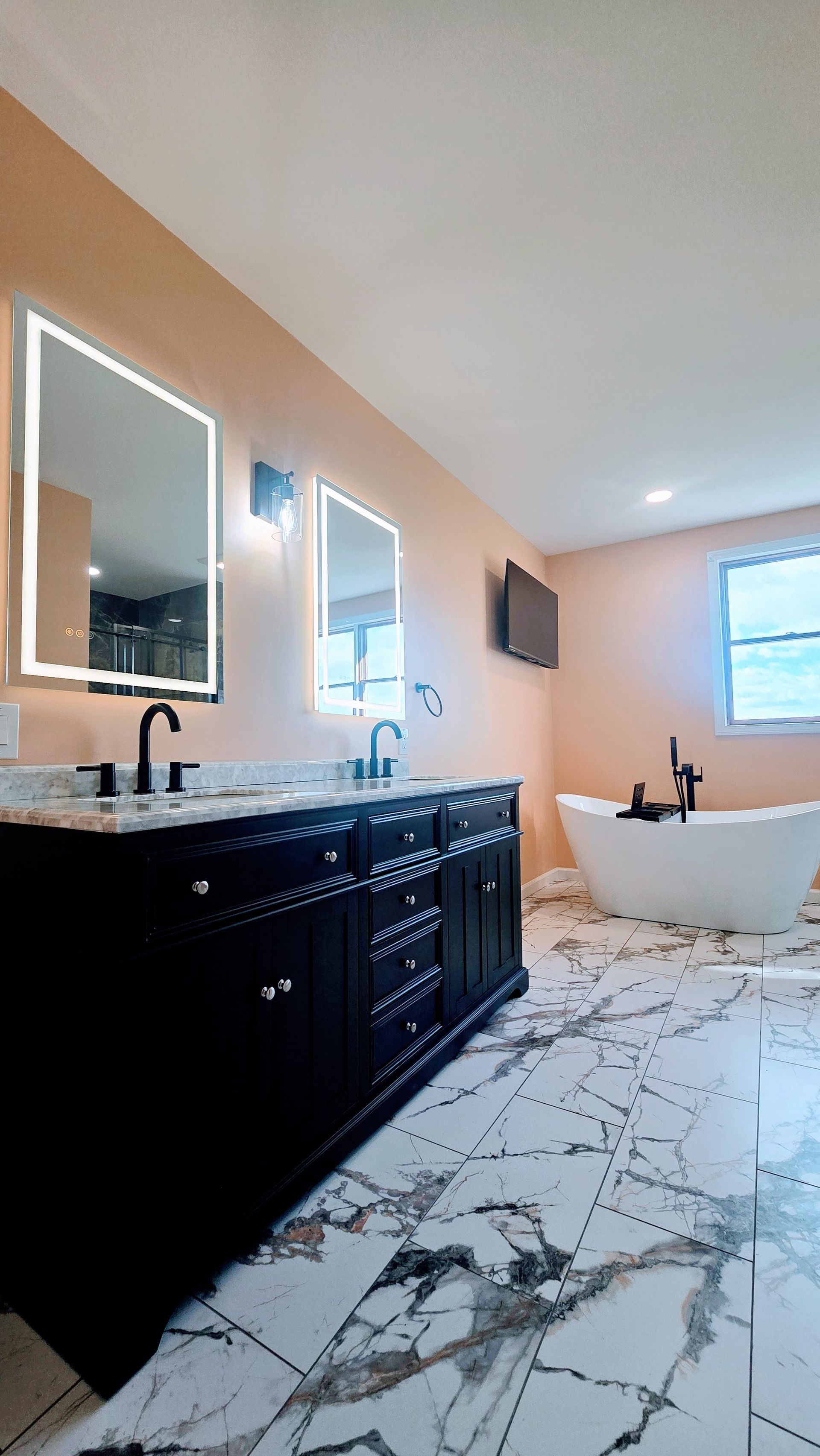 Bathroom renovation in Seymour, CT ywith black vanity, marble floor, two mirrors with LED lights, and a freestanding tub.