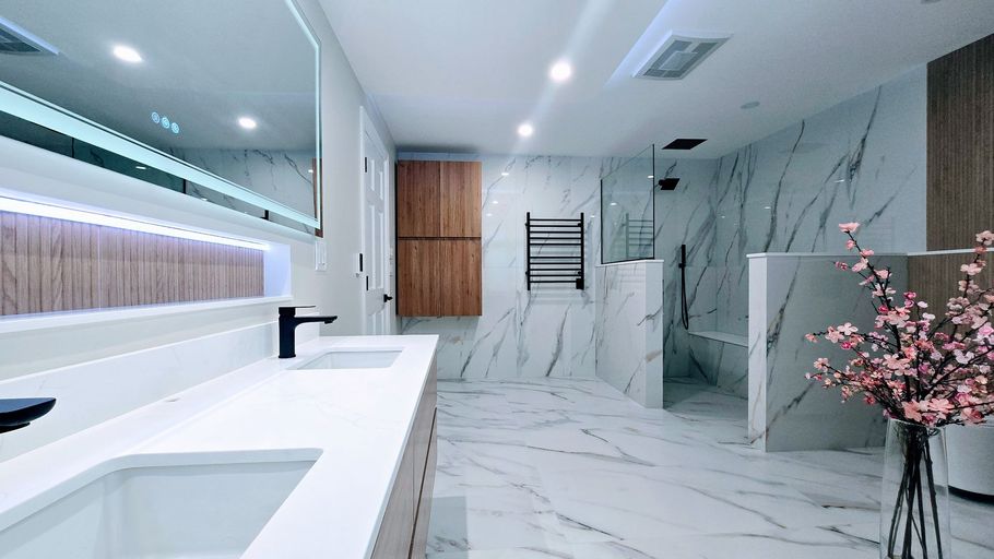 Modern bathroom remodel in Southington, CT with white marble walls, large mirror, double sink vanity, glass shower, and pink flowers.