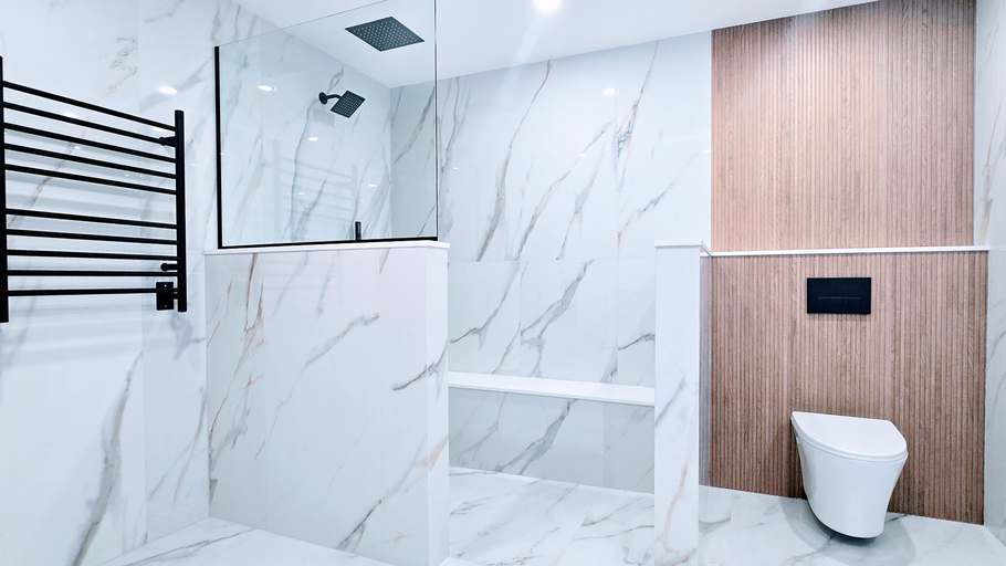 Modern bathroom remodel in Southington, CT with white marble walls, wood accent panel, black towel rack, and white toilet