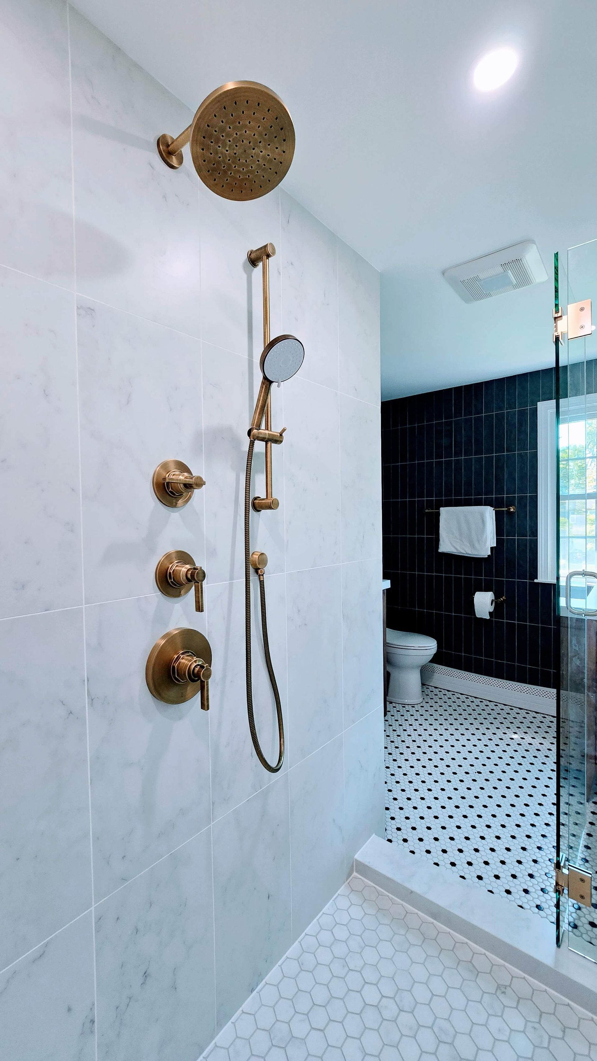Modern bathroom shower in Glastonbury, CT with gold fixtures, white tiled walls, and black-and-white hex floor tiles