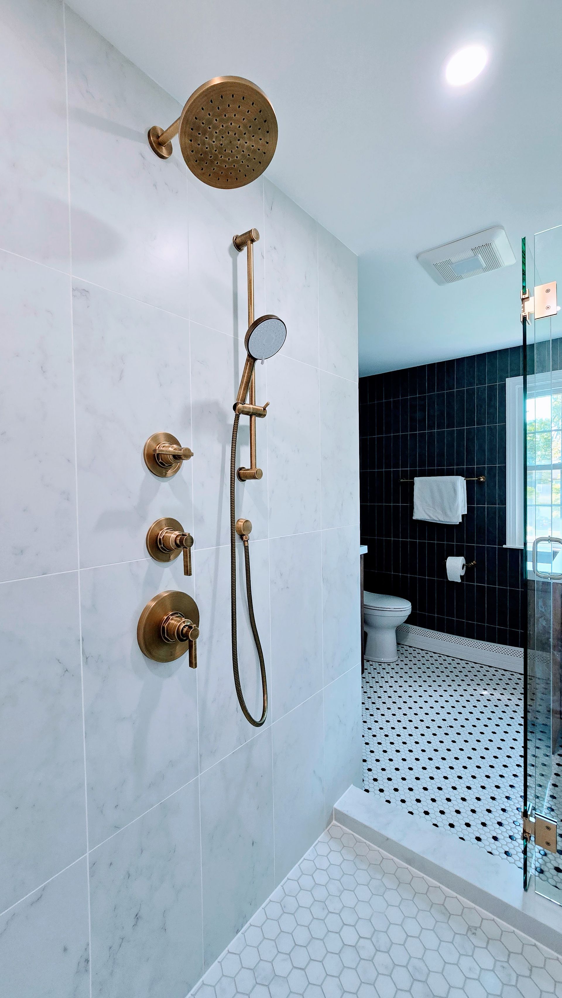 Modern bathroom with white tile, brass shower fixtures, and black accent wall. By First Choice Bathroom Remodeling done in Glastonbury CT.