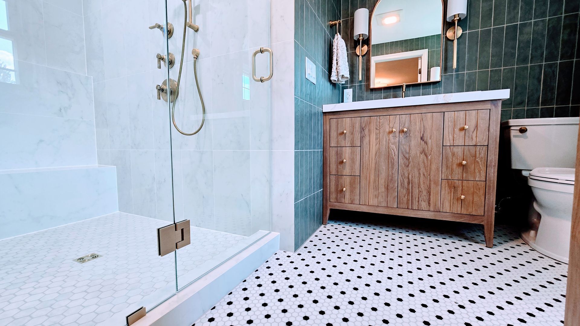 Modern bathroom with glass shower, white tile floor, and wooden vanity with sink and mirror. By First Choice Bathroom Remodeling done in Glastonbury CT.