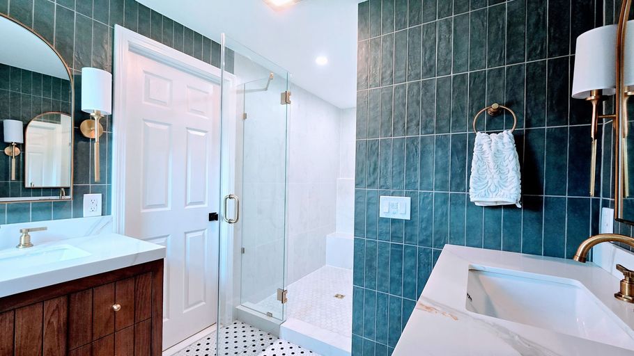 Modern bathroom in Glastonbury, CT with dark tile walls, white vanity, glass shower door, and a freestanding tub.