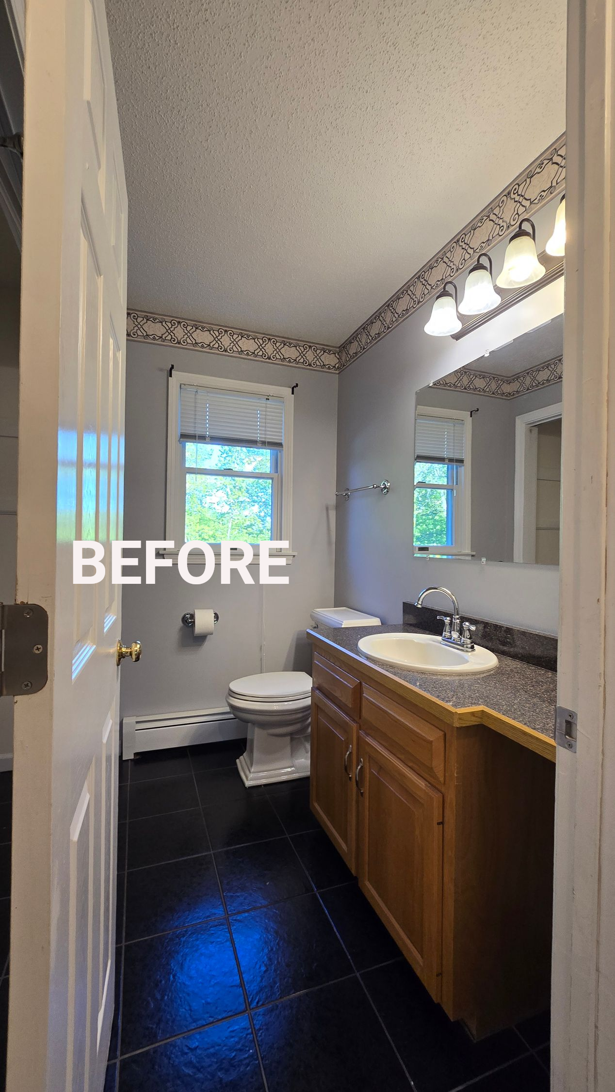 Small bathroom with dark floor, wood vanity, toilet, mirror, and window near the sink.