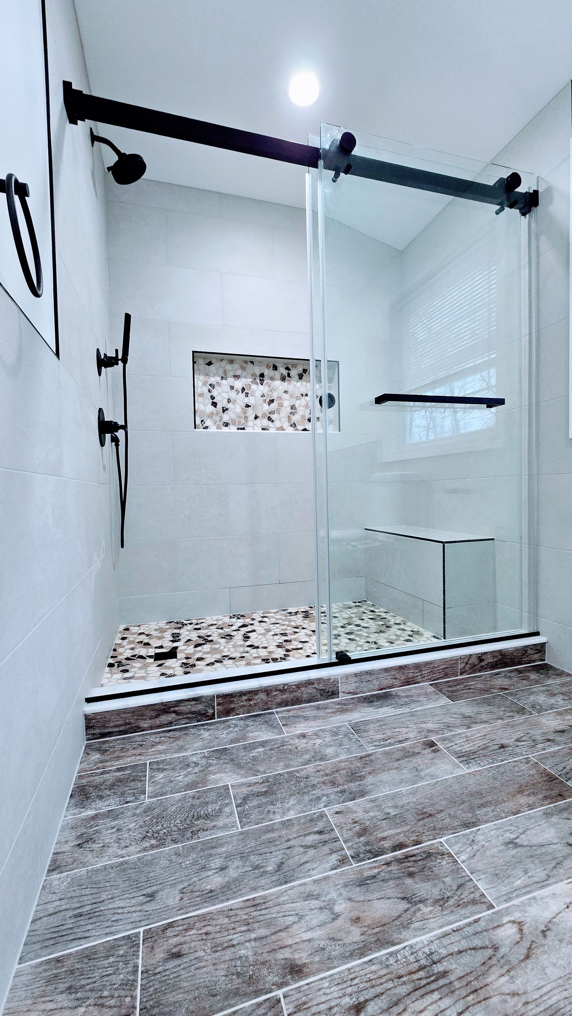 Modern bathroom in Berlin, CT completed by First Choice Bathroom Remodeling with a glass shower enclosure, black fixtures, and pebble stone accents.