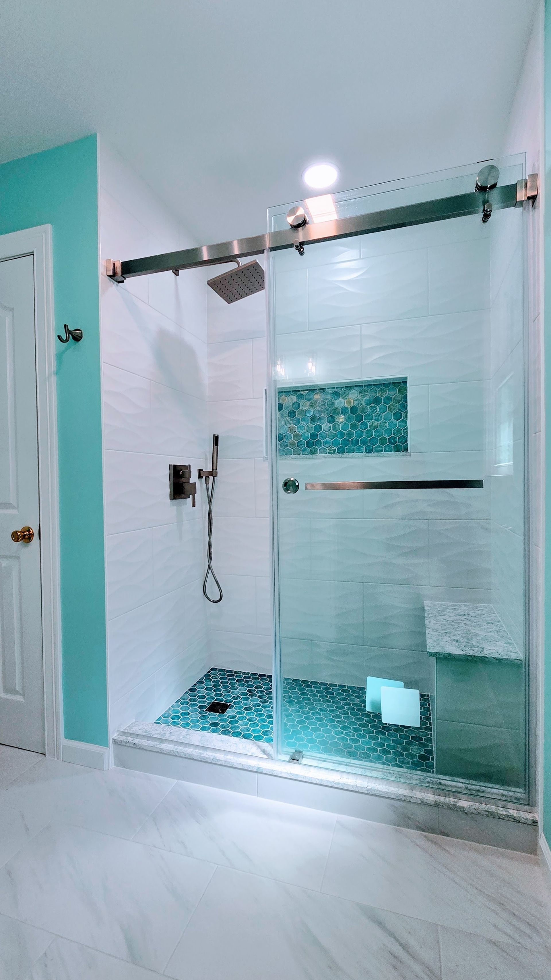 Glass shower with turquoise tile accents and white bathroom walls next to an open door. Southbury CT