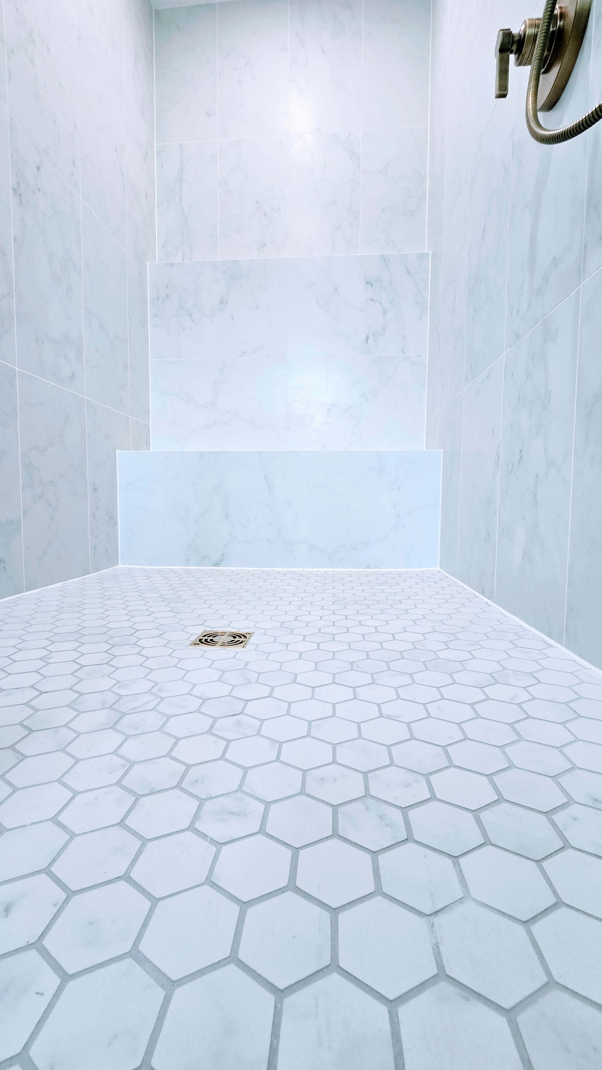 Empty white tiled shower stall in Glastonbury, CT with hexagon floor tiles and pale blue walls