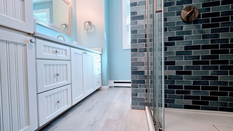 Bathroom with white cabinets, blue walls, dark tiled shower, and light wood-look flooring.