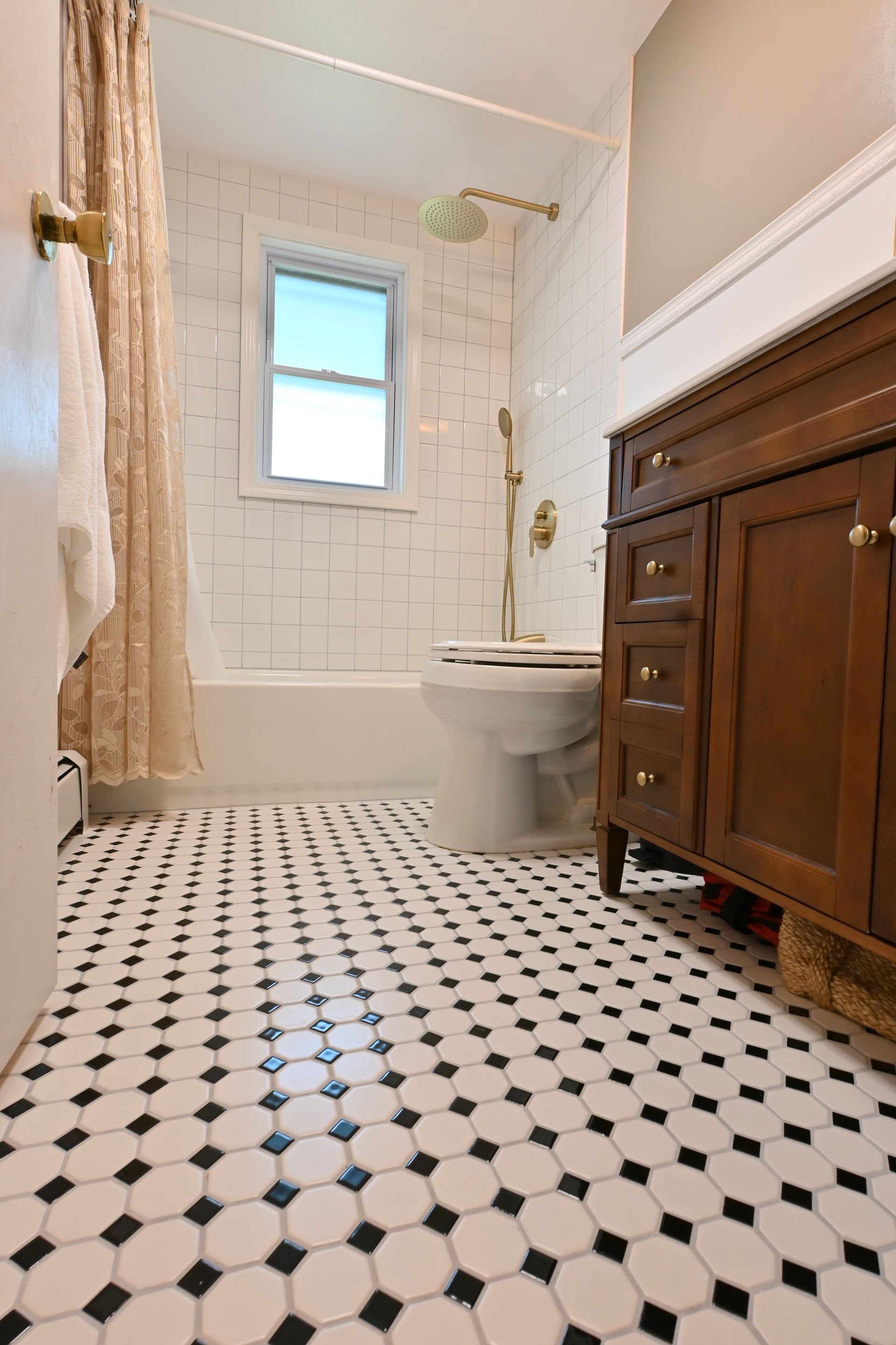 Small bathroom with black-and-white tile floor, white walls, sink, toilet, and wooden vanity.
