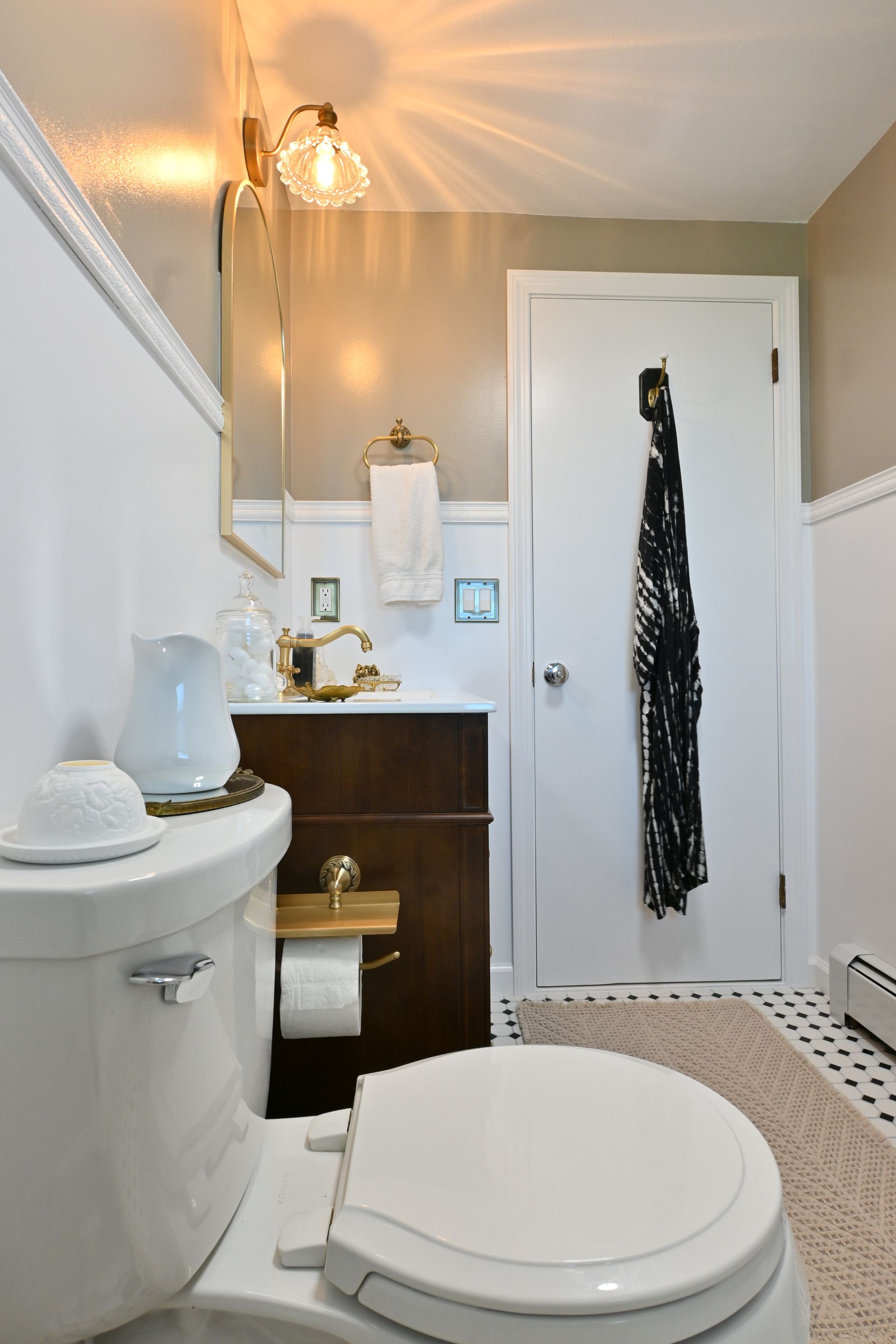 Small bathroom with white toilet, dark vanity, mirror, and a black robe on the door.