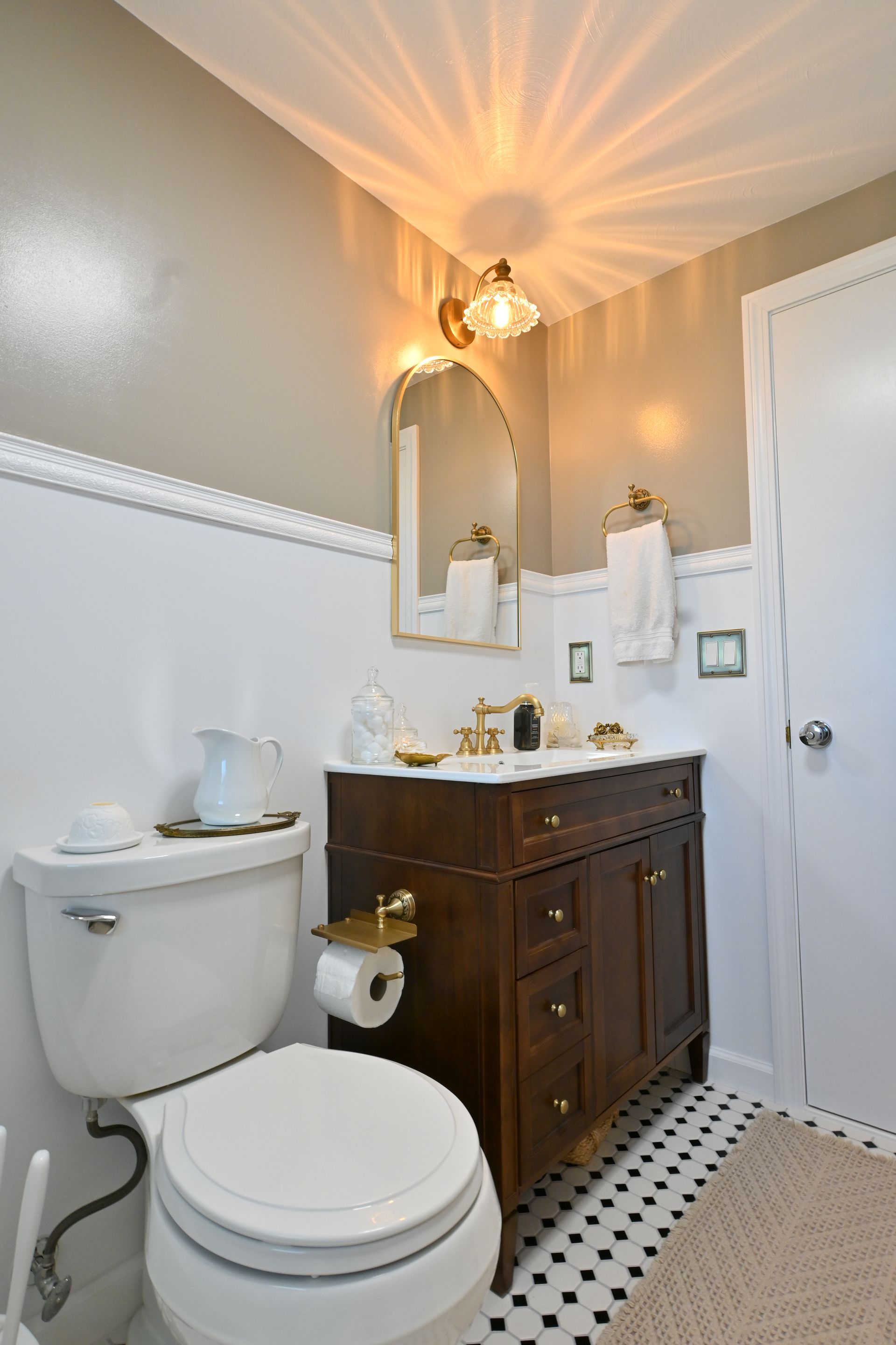 Small bathroom with white toilet, dark wood vanity, mirror, and beige walls lit by warm light.