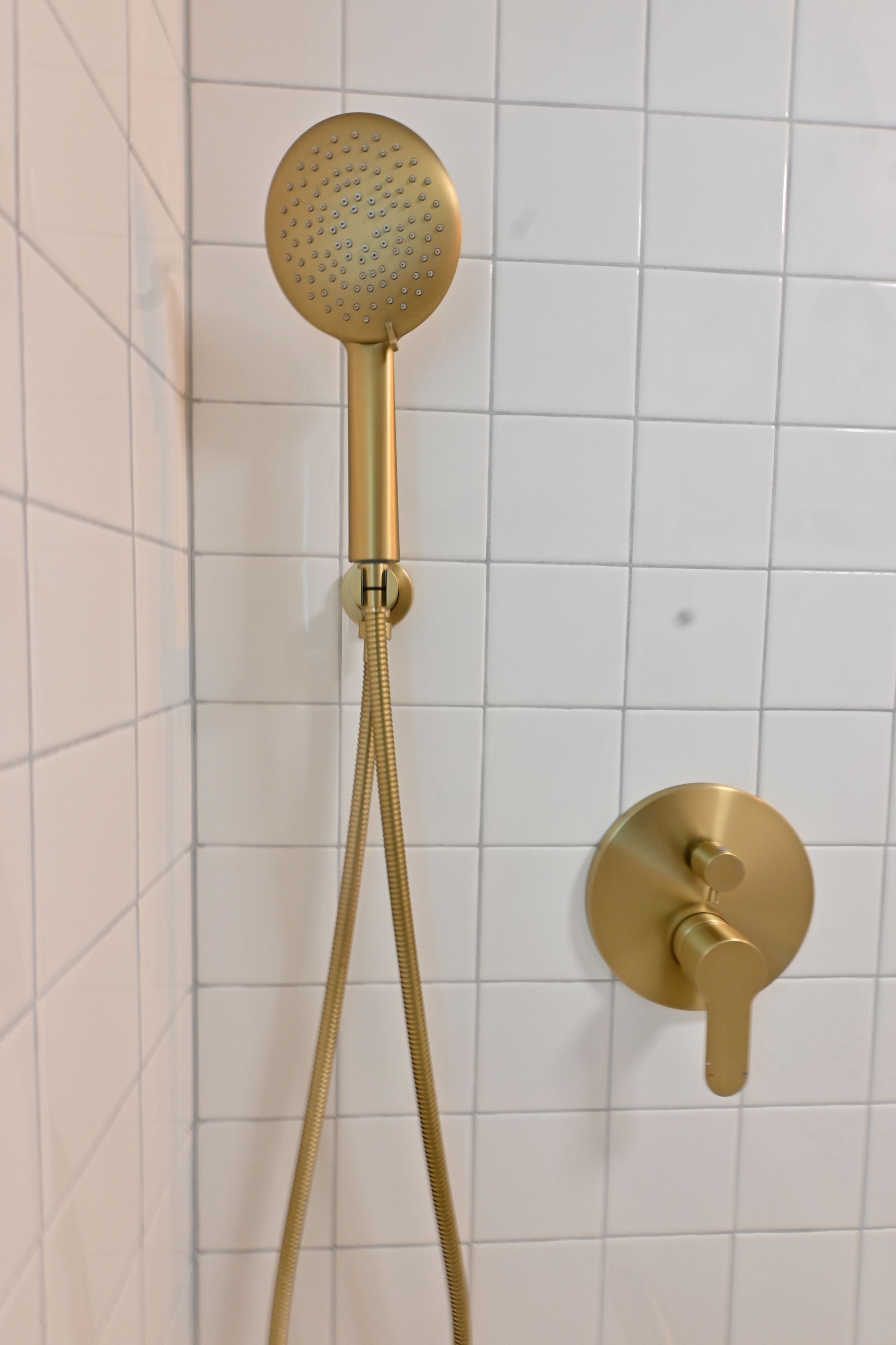 Gold shower head and handheld shower hose in a white tiled bathroom