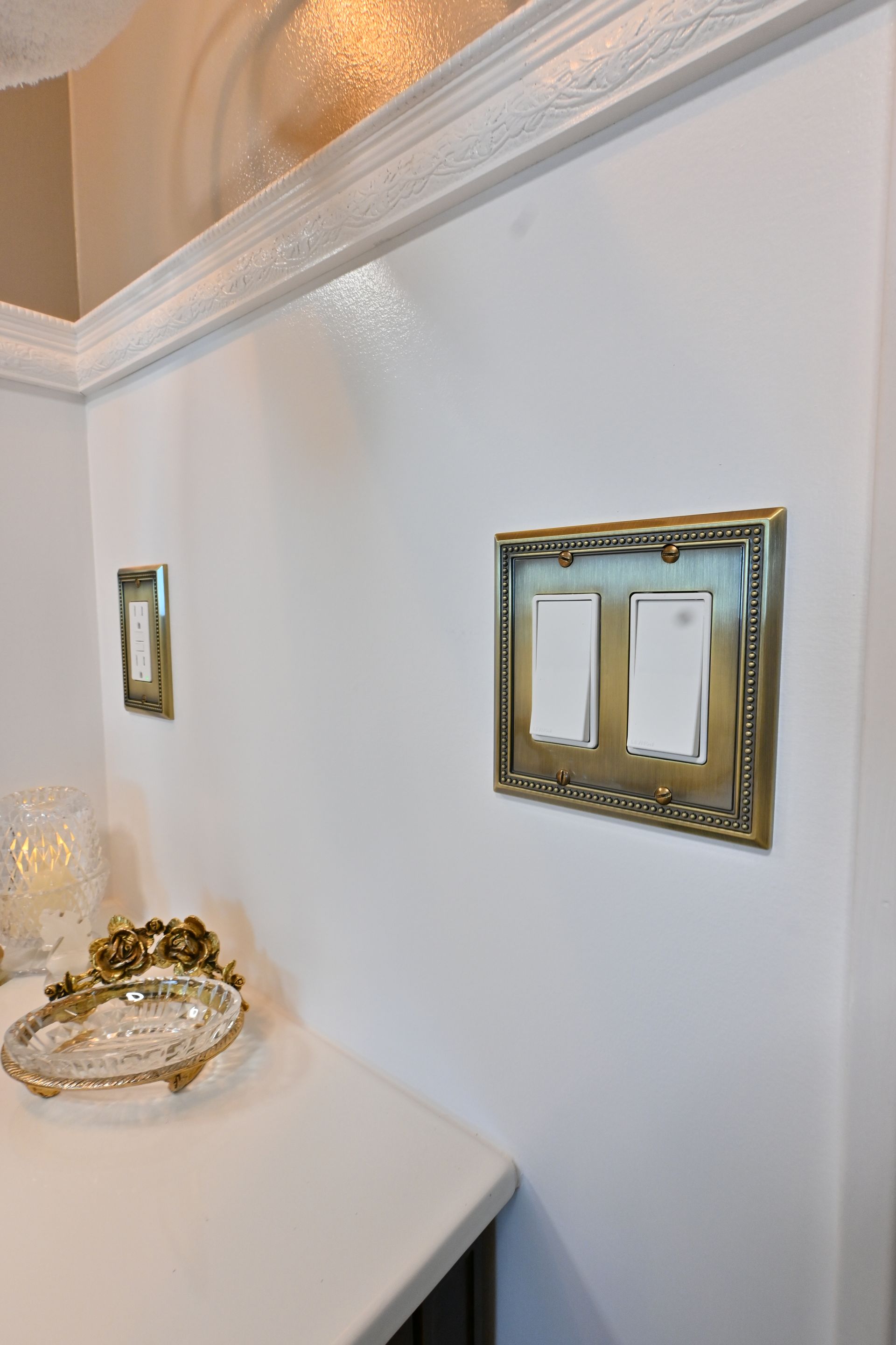 White wall with gold light switch plates and a white countertop in a decorative interior corner.