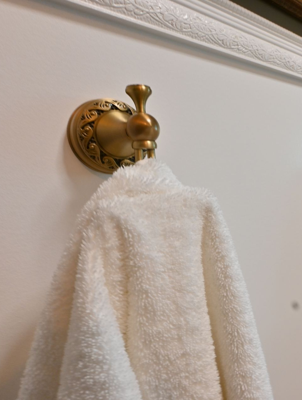 White towel hanging on a gold wall hook against a beige wall.