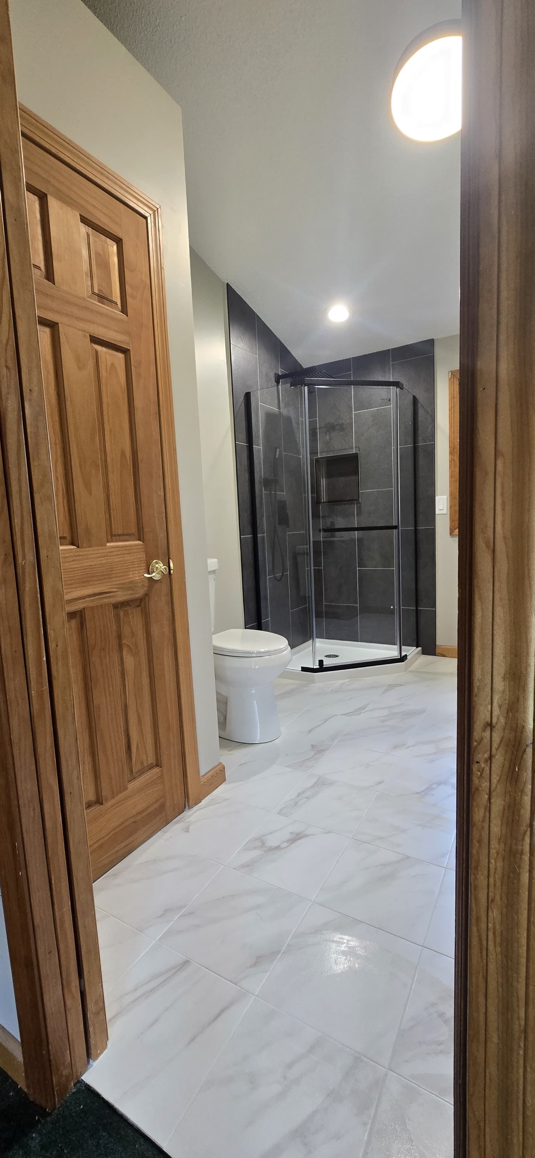 Narrow hallway with marble floor, wooden doors, and a bright light at the far end. By First Choice Bathroom Remodeling done in Cheshire, CT.