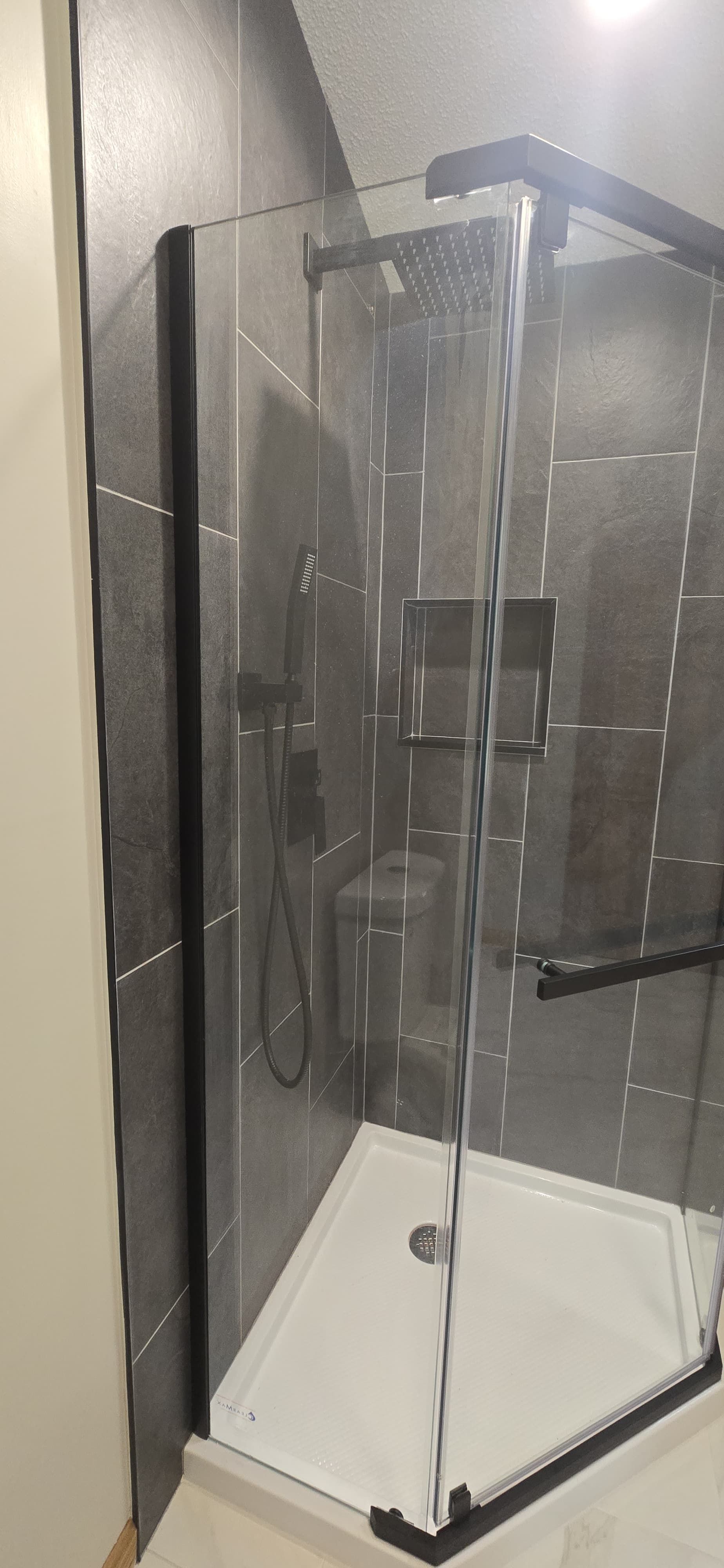 Glass shower enclosure with black trim in a tiled bathroom. By First Choice Bathroom Remodeling done in Cheshire, CT.