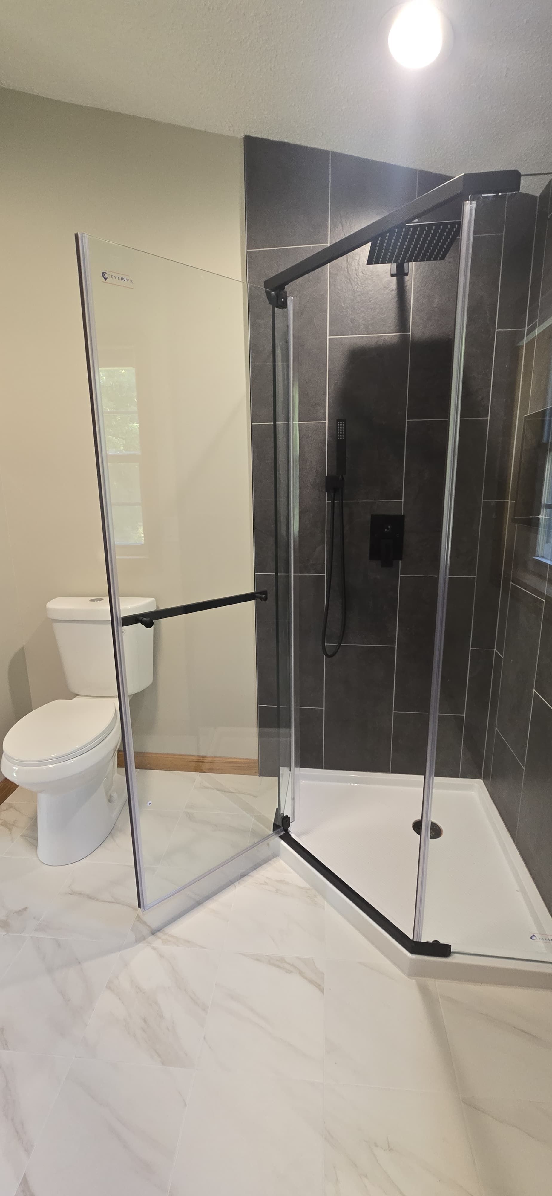 Small bathroom with a glass shower enclosure, toilet, and marble tile floor. By First Choice Bathroom Remodeling done in Cheshire, CT.