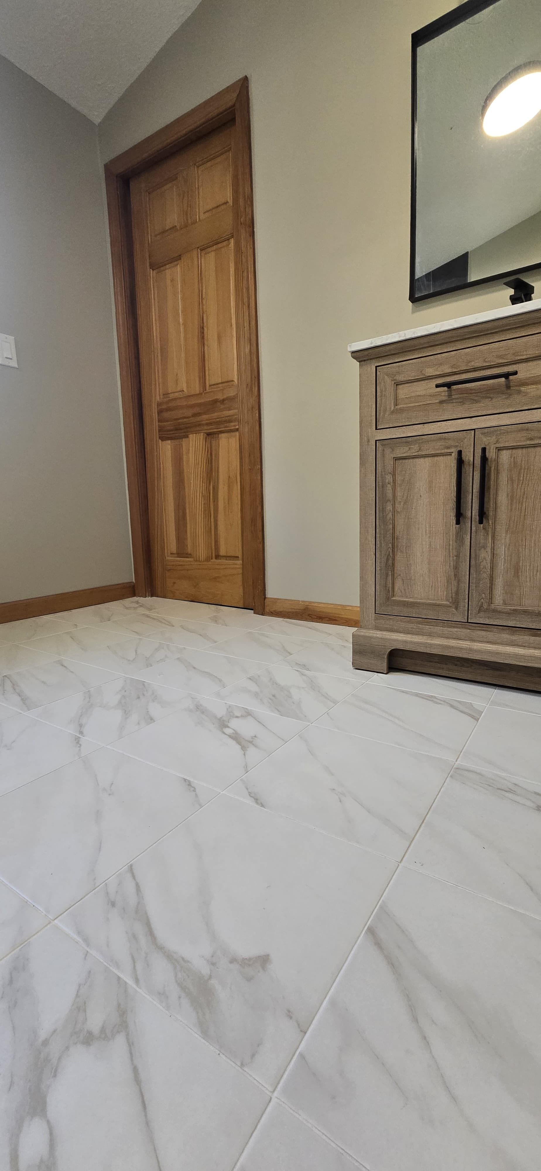 Modern room with white marble floor, wooden door, and carved cabinet with mirror. By First Choice Bathroom Remodeling done in Cheshire, CT.
