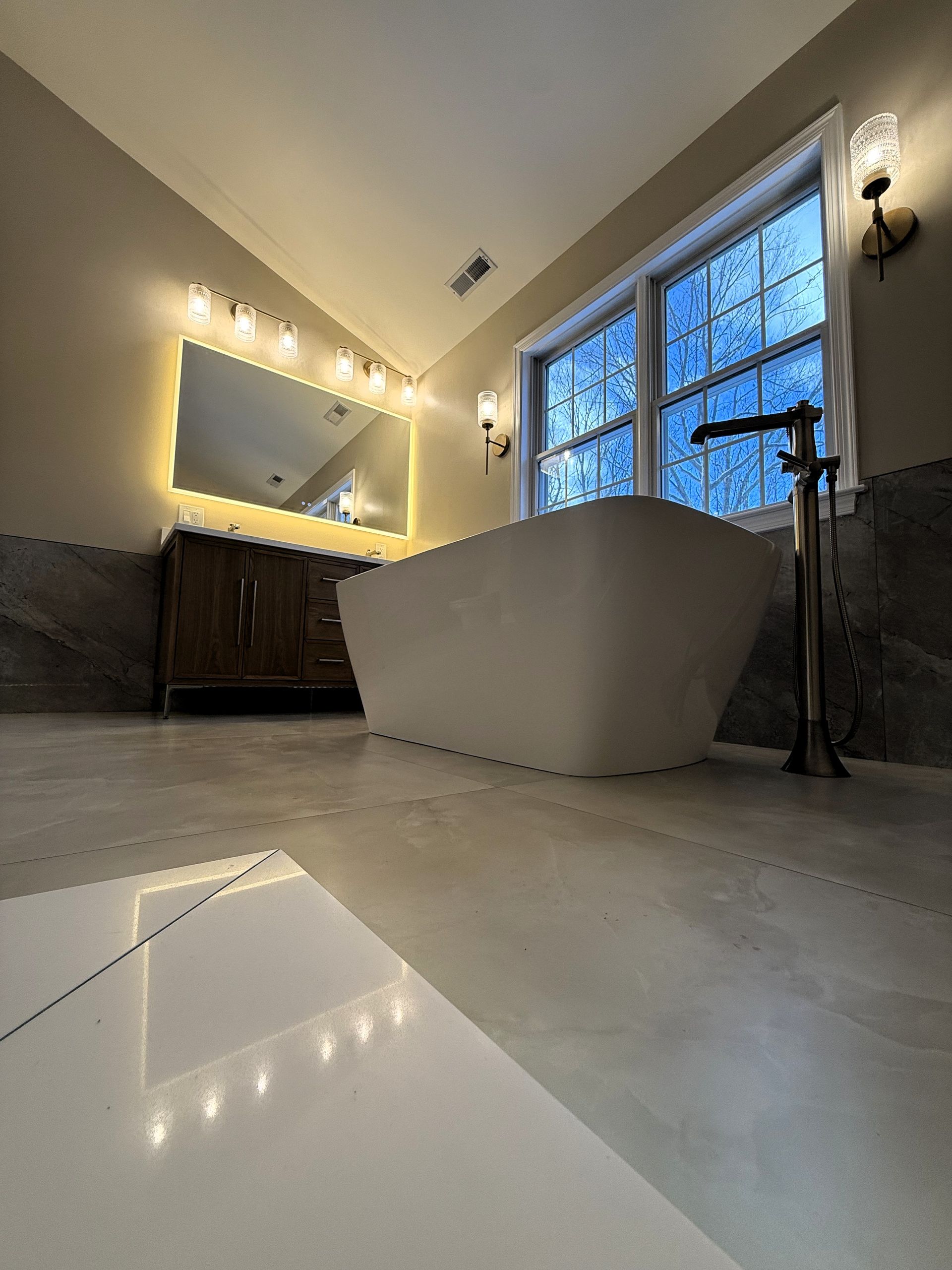 Modern bathroom remodel in Glastonbury, CT with freestanding tub, large mirror, and window with natural light.