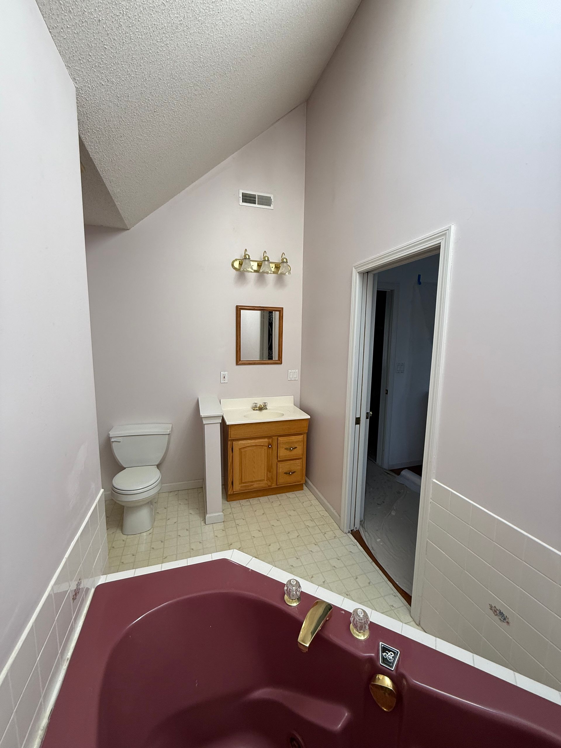 Bathroom with maroon tub, pink walls, wooden vanity, and open door.