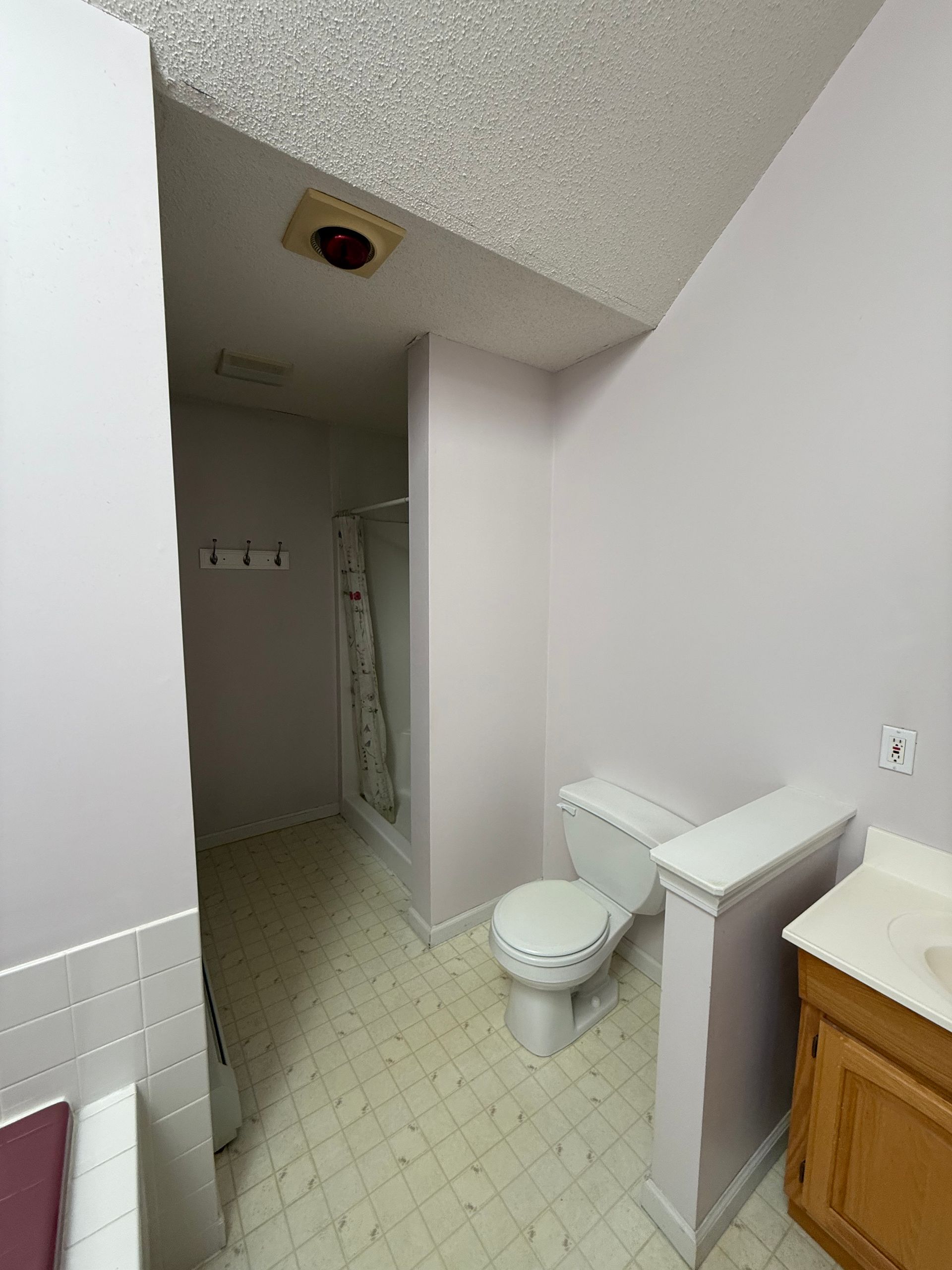 Bathroom with pale pink walls, a toilet, shower, and a vanity with a wooden cabinet.