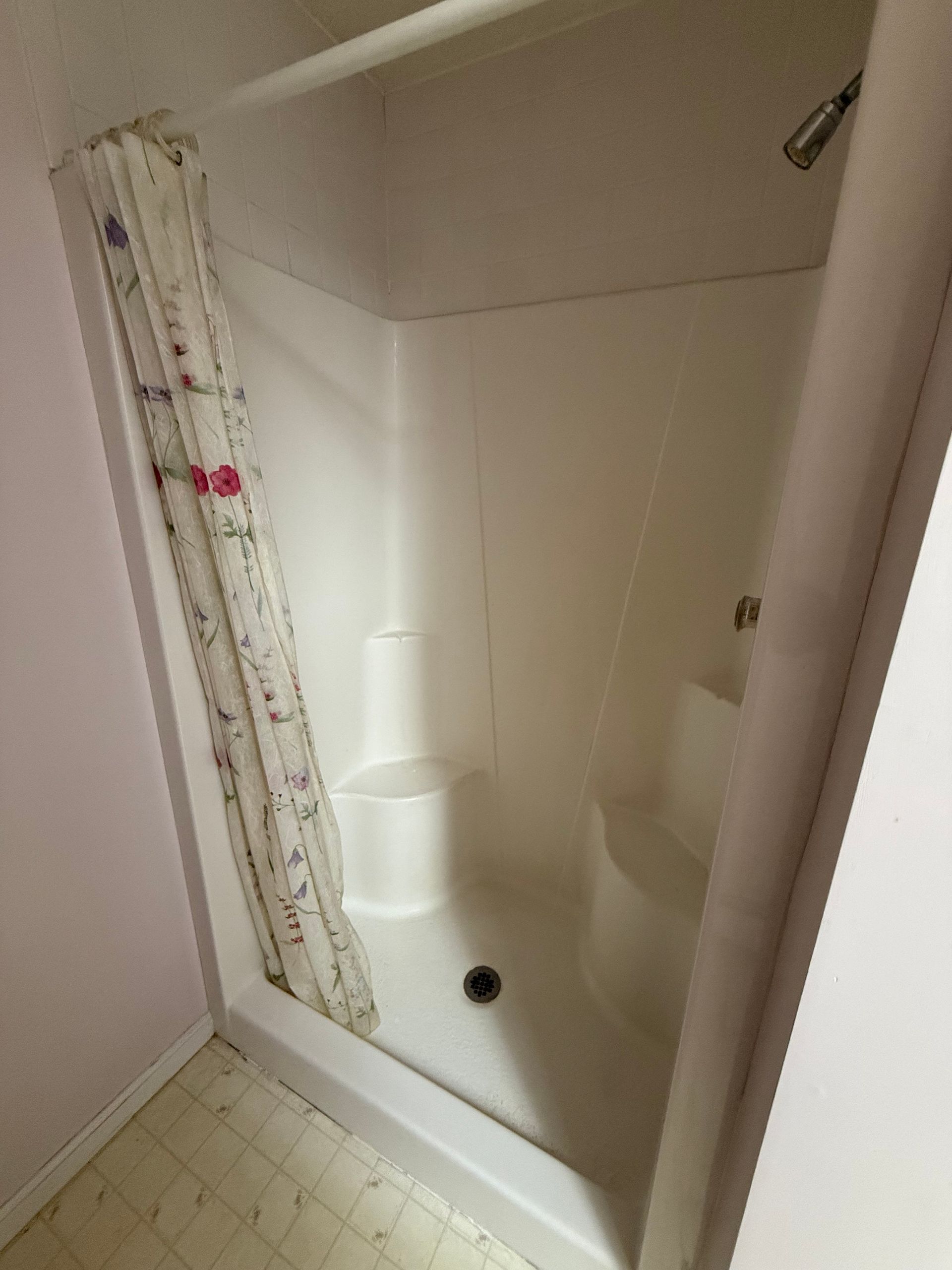 A white shower stall with a floral shower curtain in a bathroom.