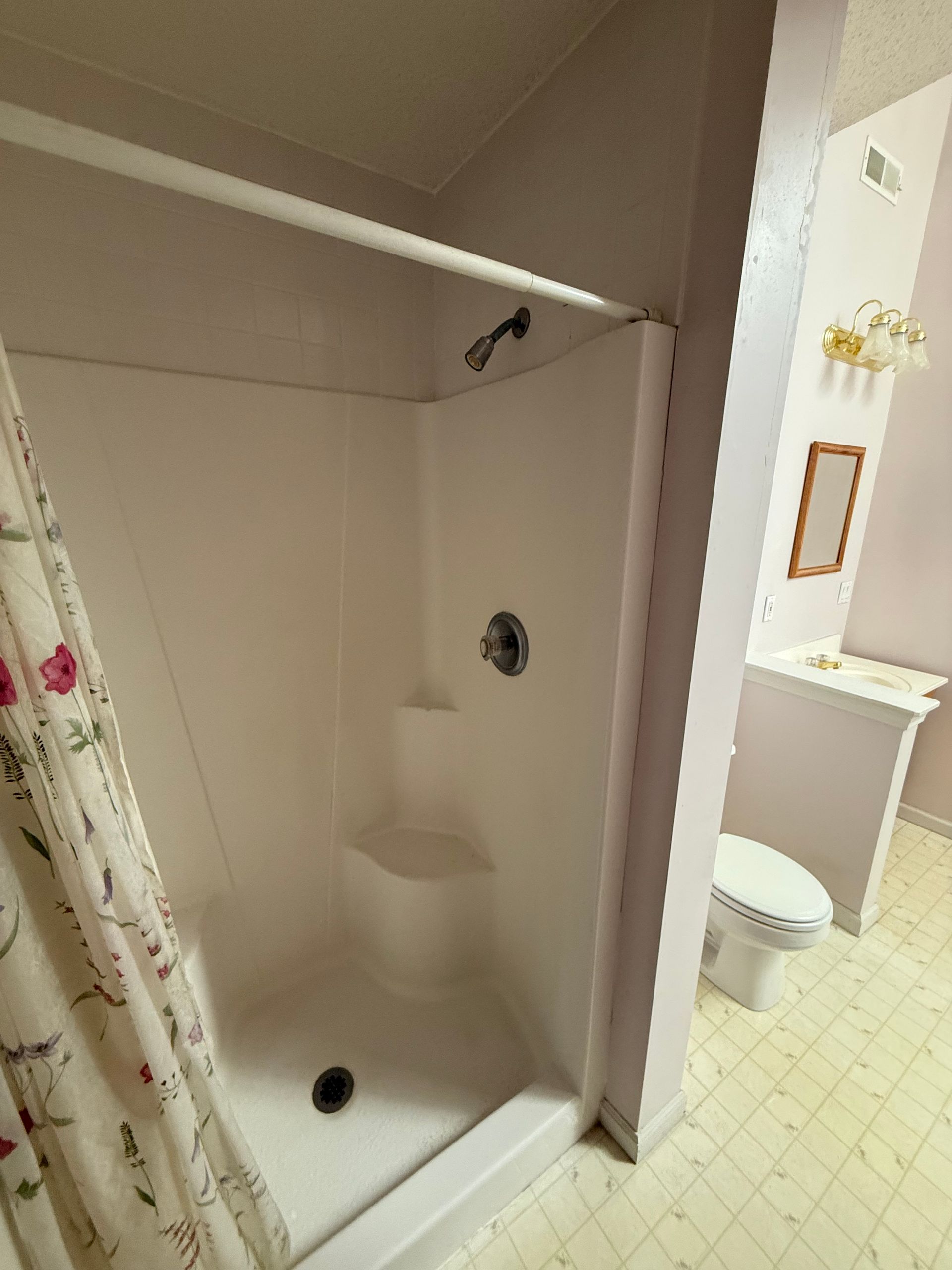 A bathroom with a shower , toilet , sink and mirror.