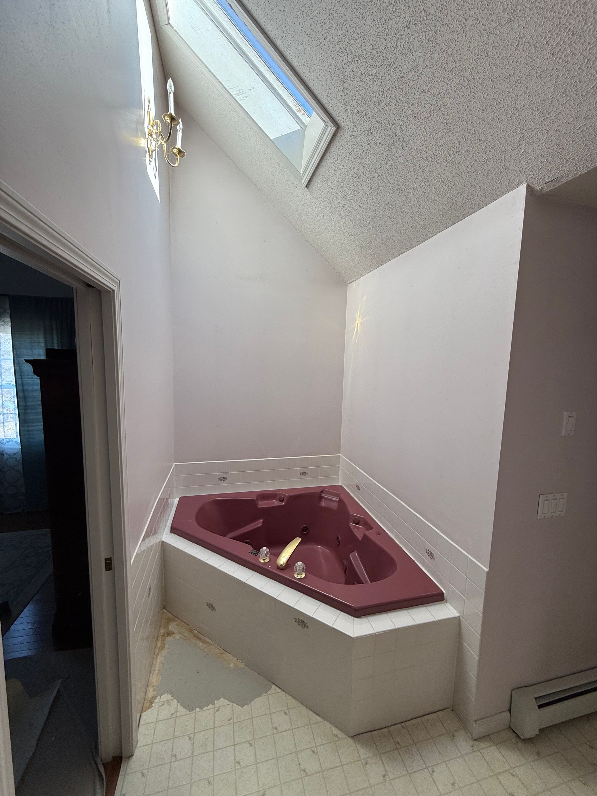 A bathroom with a red jacuzzi tub and a skylight.