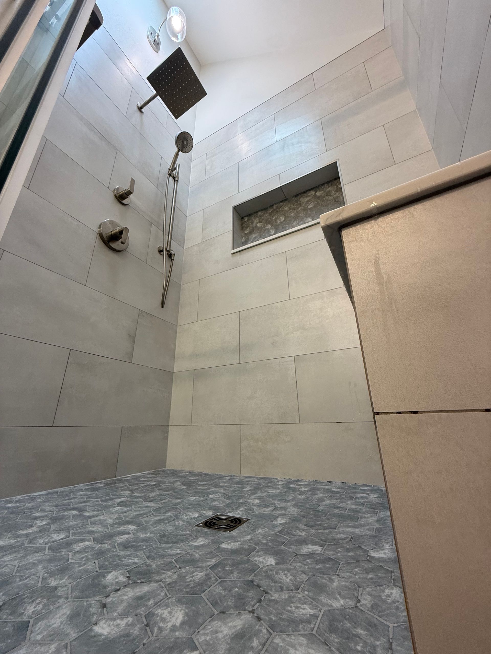 Gray-tiled shower with rain showerhead, niche, and pebble floor. Beige corner cabinet.