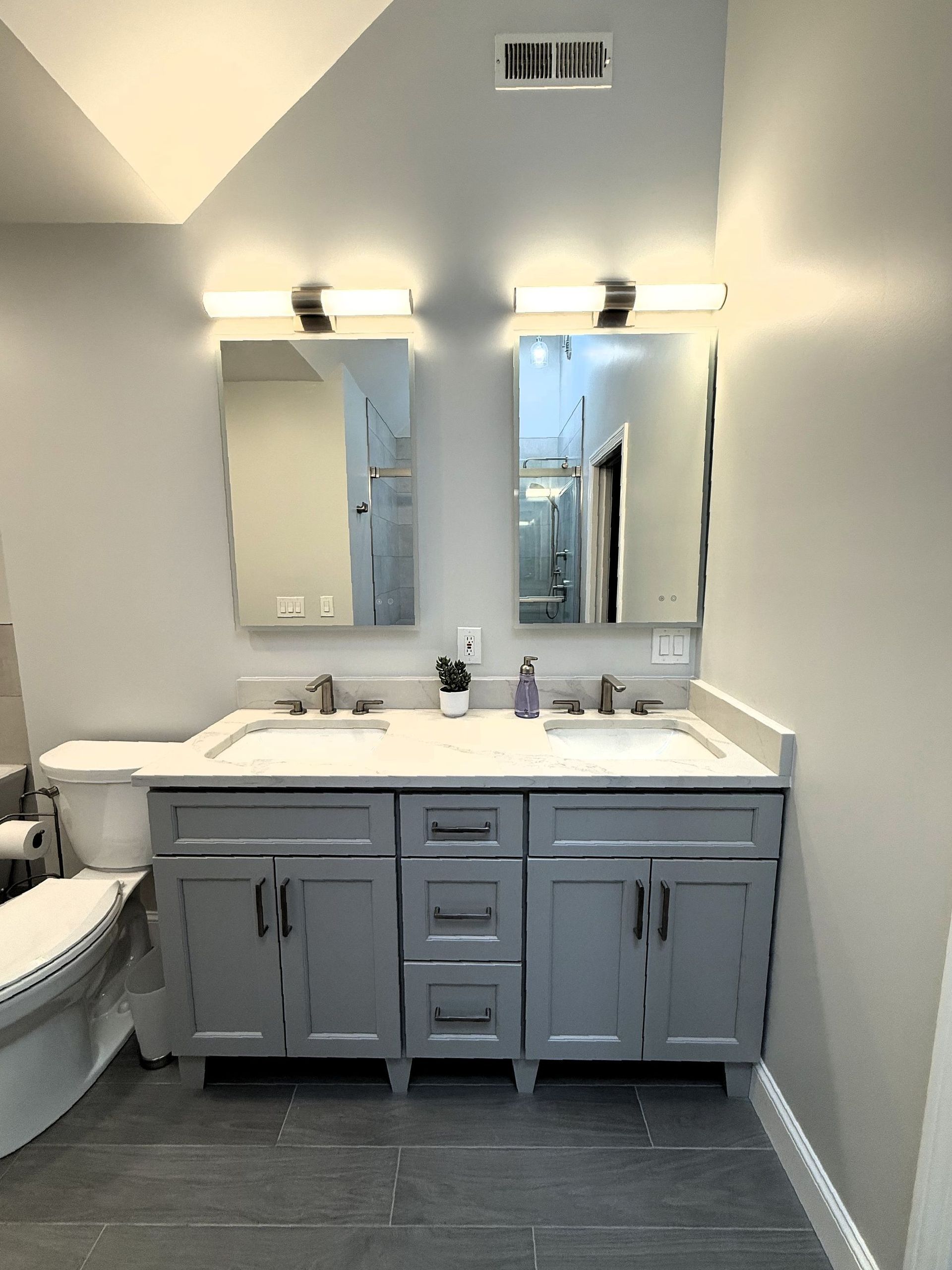 A bathroom with two sinks and two LED mirrors.