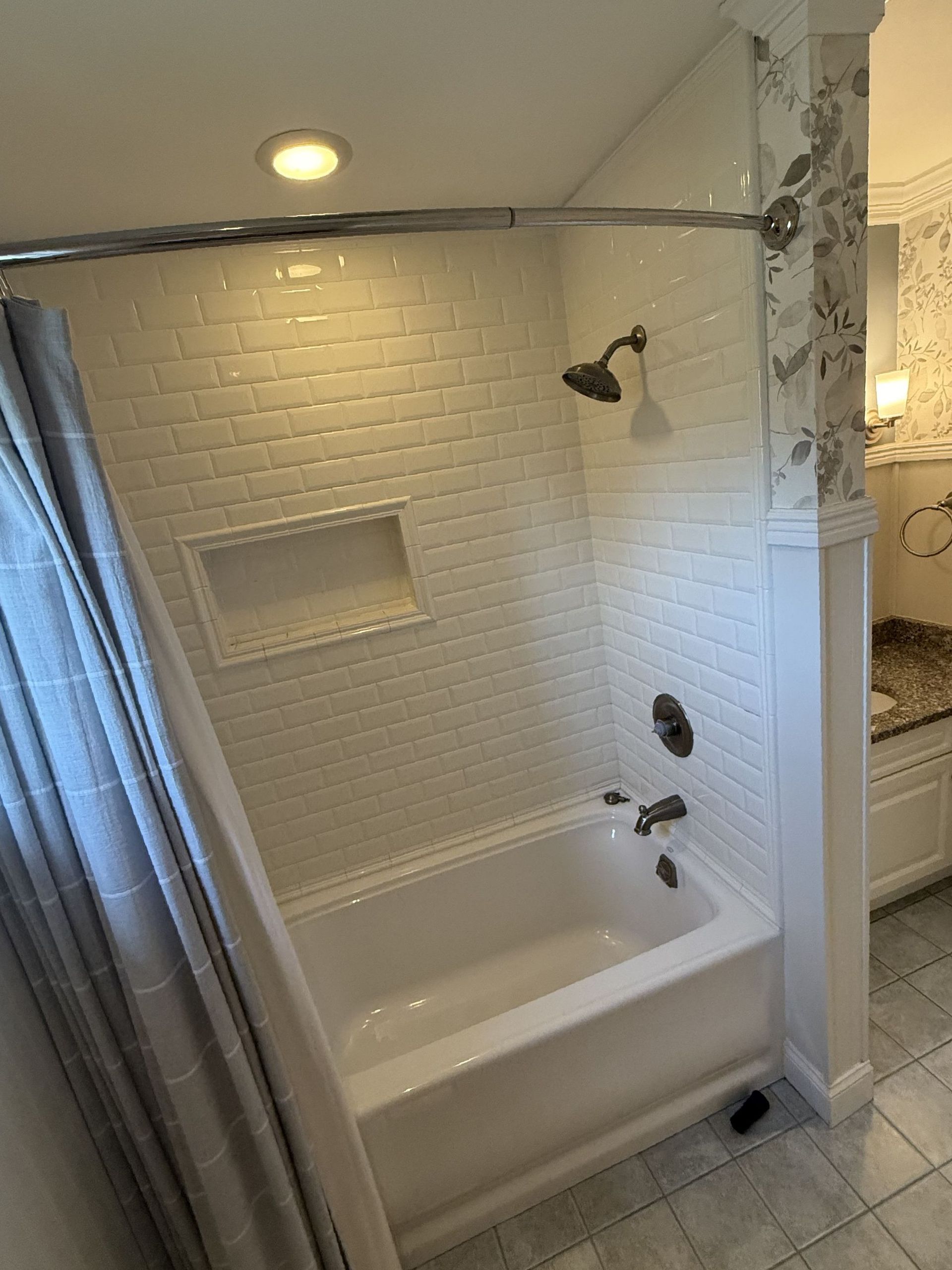 White tiled bathroom with a bathtub, showerhead, and a gray shower curtain.
