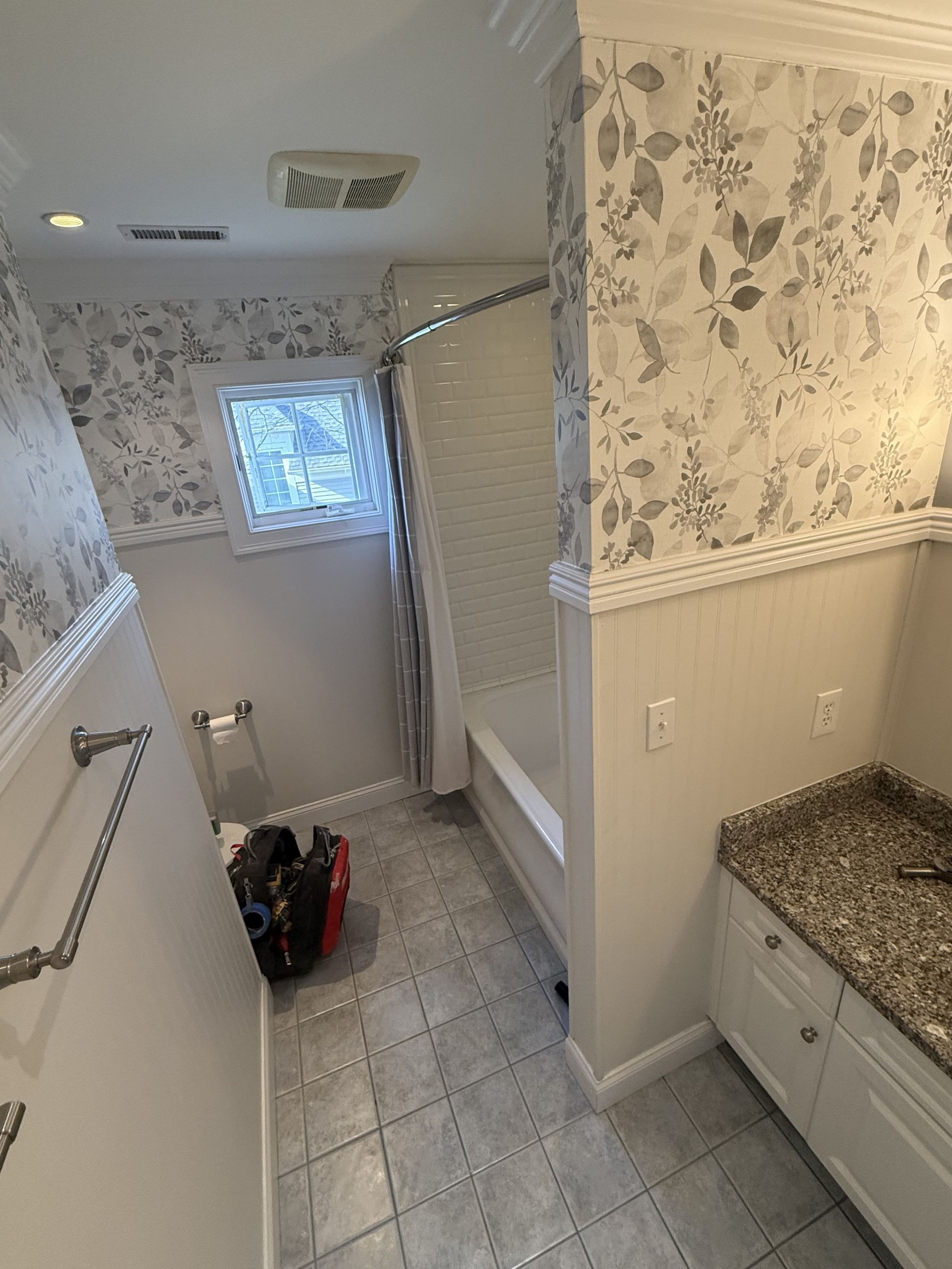 Bathroom with floral wallpaper, white beadboard, gray tile floor, and granite countertop.