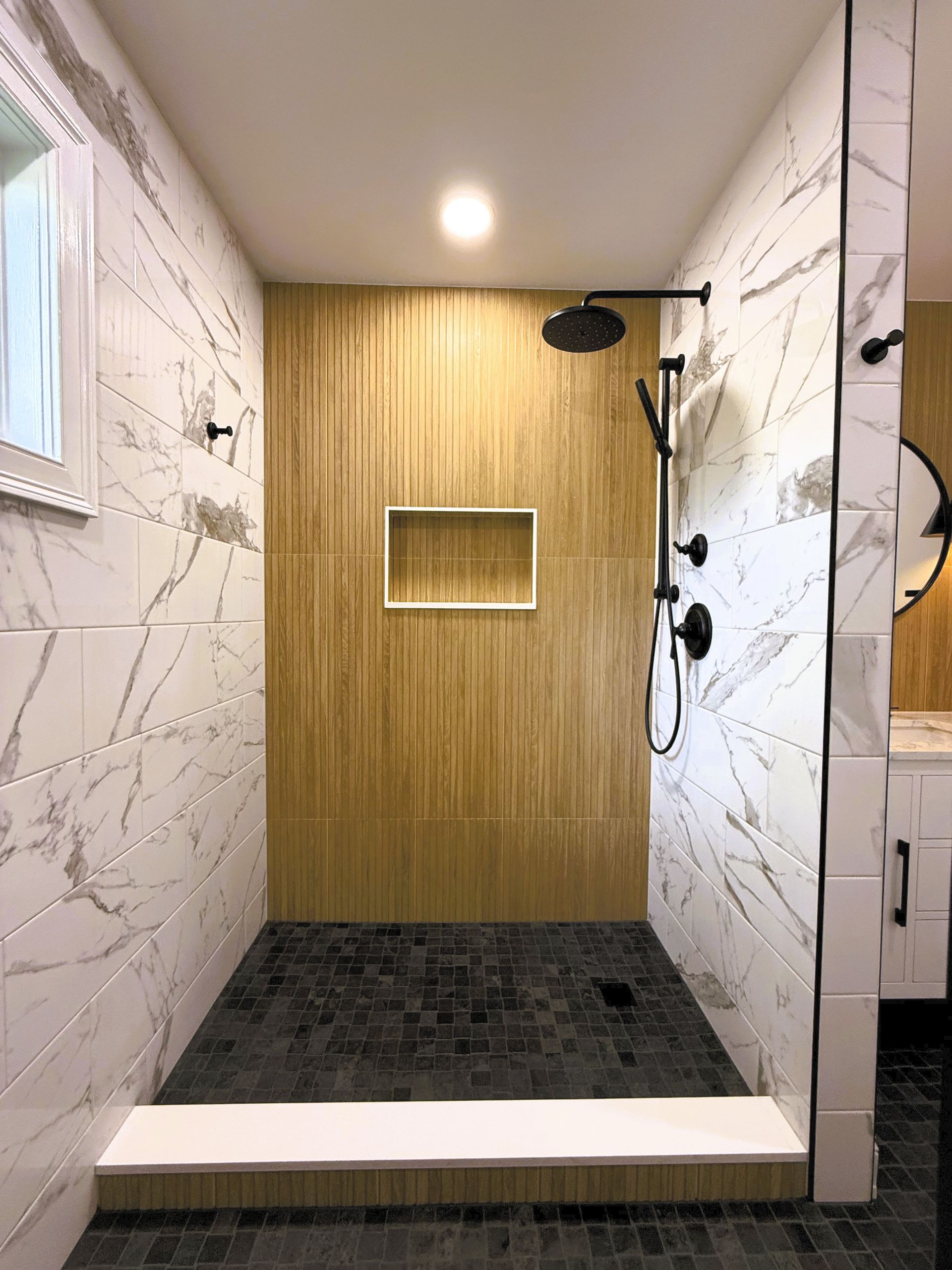 Modern shower with marble walls, gold accent wall, and dark floor. Black showerhead and fixtures.