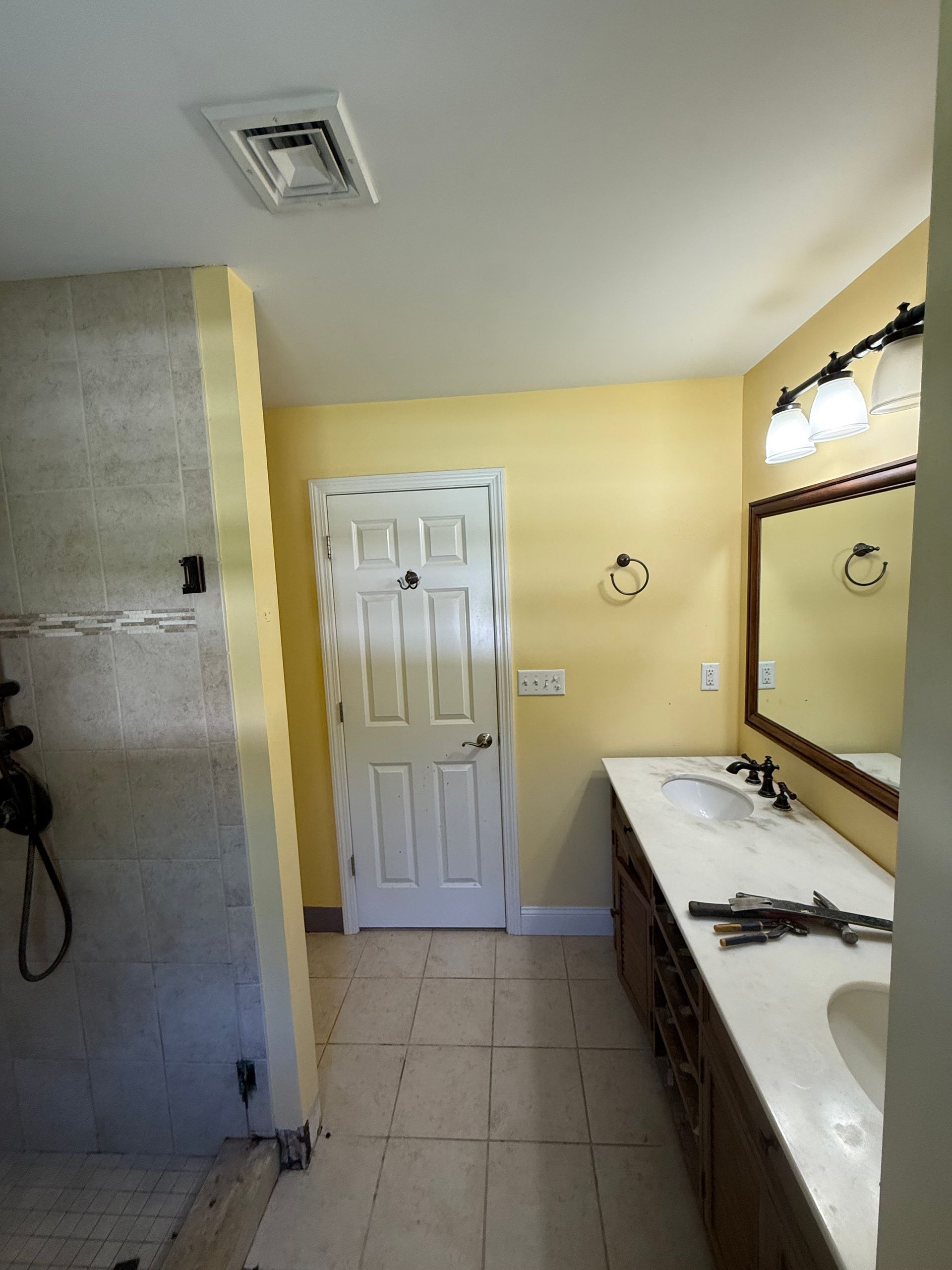 Bathroom with yellow walls, white door, vanity with two sinks, and tiled floor.