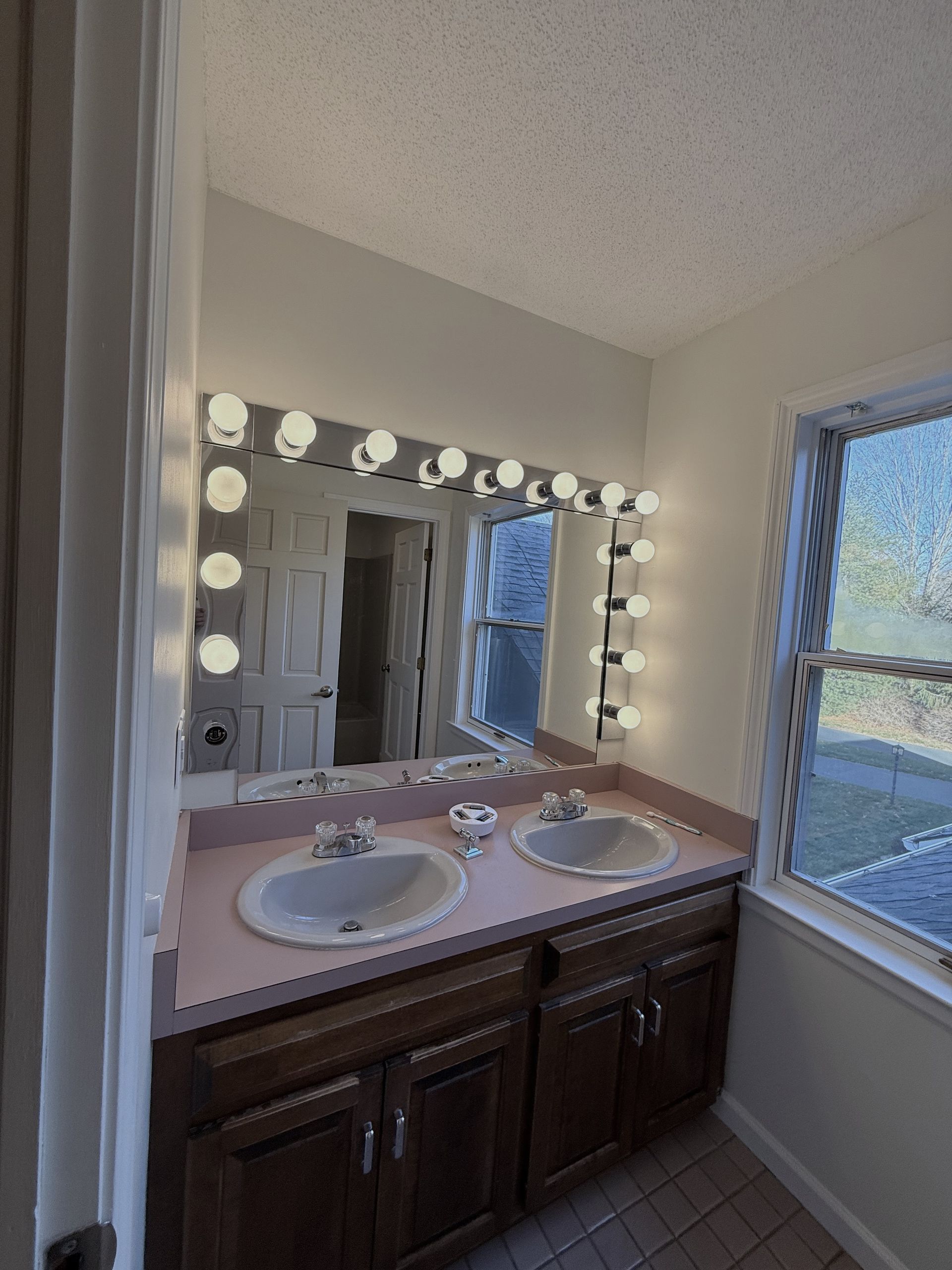 Bristol Bathroom with double sinks, lit mirror, wooden cabinets, and window.